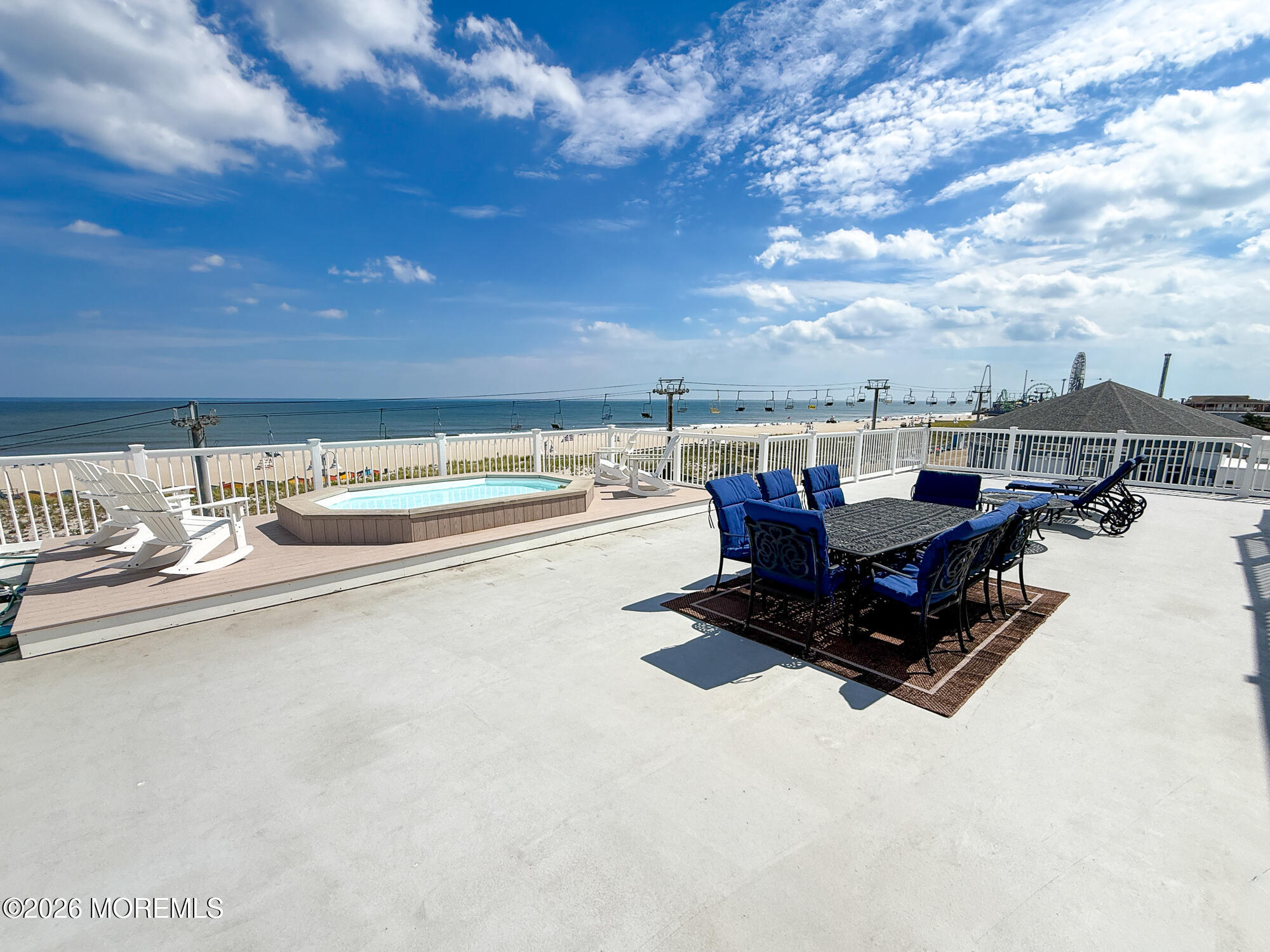 Rooftop terrace with a hot tub and outdoor dining set overlooking the beach and ocean.