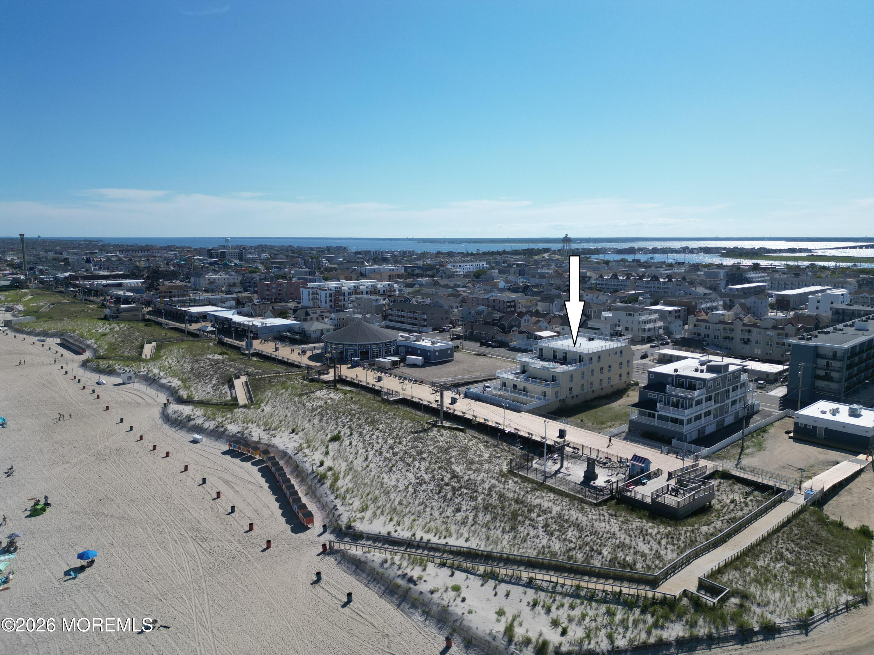Aerial beachfront property marked by an arrow, beside a boardwalk, sandy beach, and ocean.