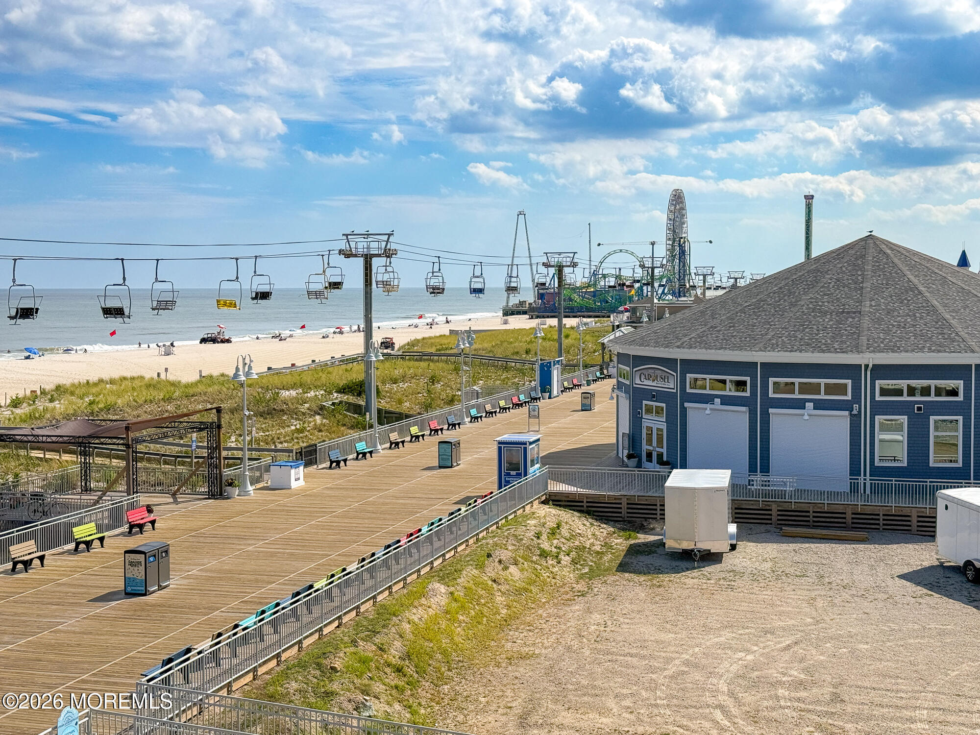 Beach and boardwalk beside the ocean, with a chairlift, amusement rides, and a blue carousel building.