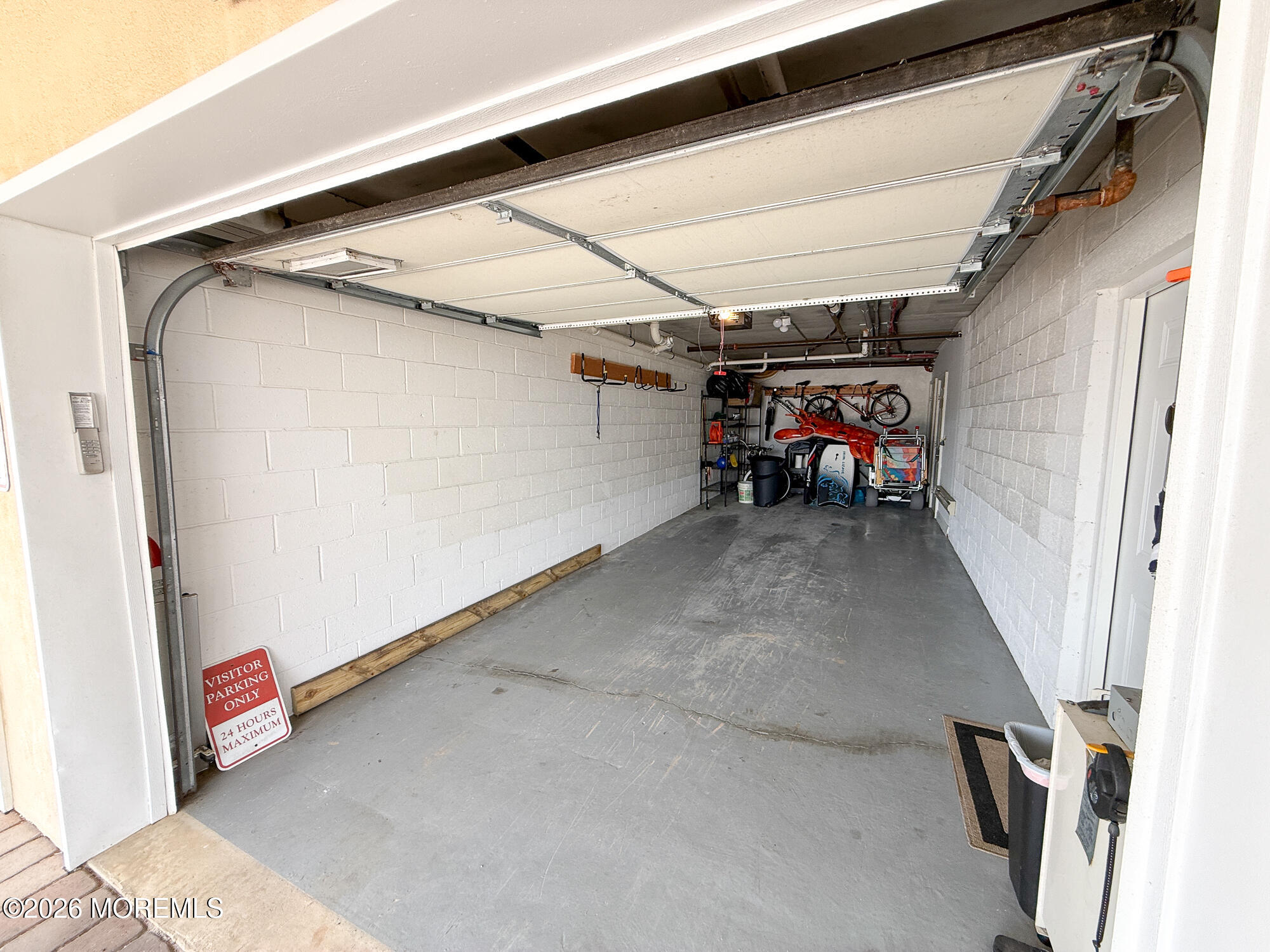 Single-car garage with a raised door, concrete floor, and bicycles and kayaks stored at the far end.