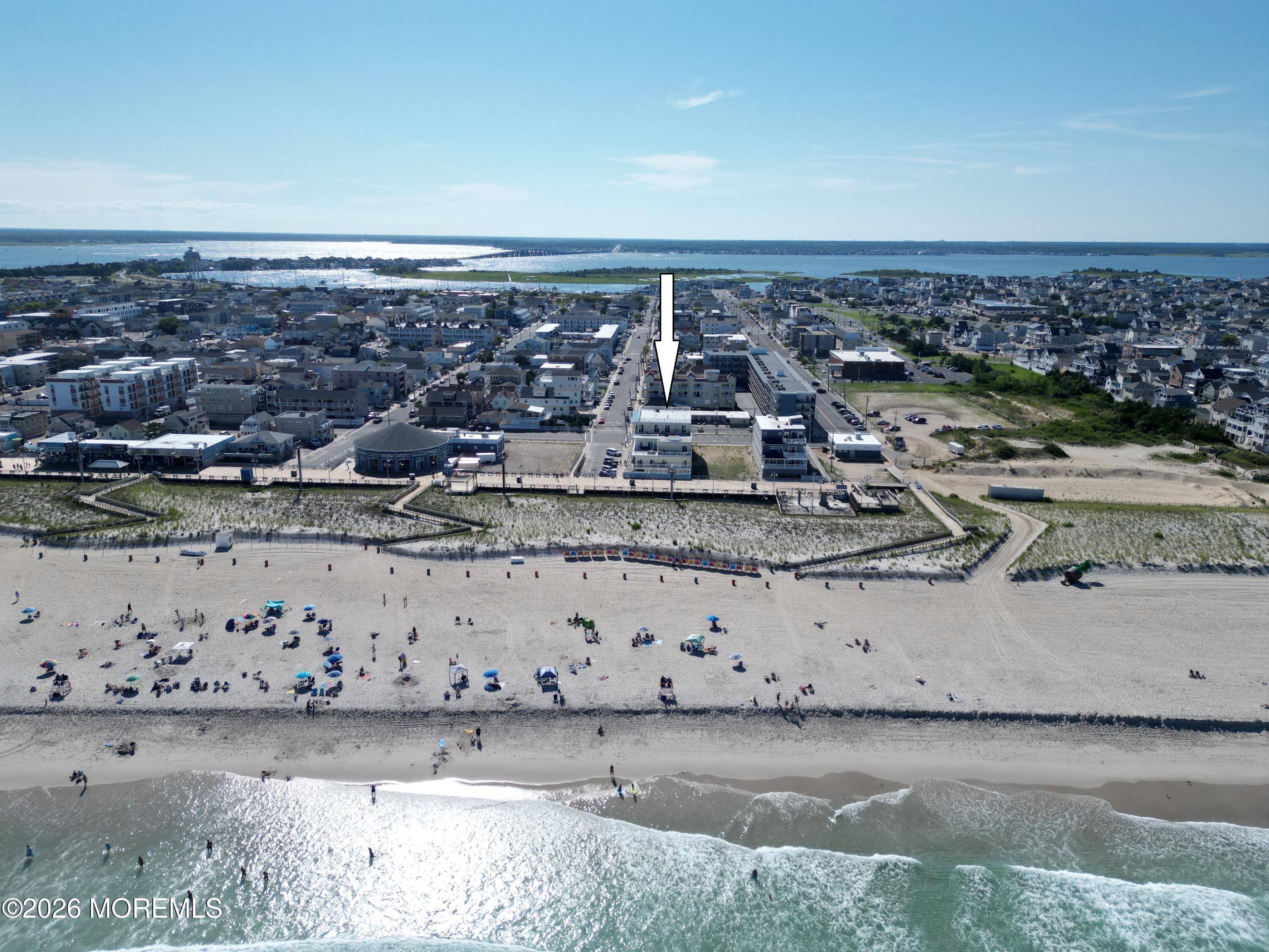 Aerial view of the beachfront building marked by an arrow, with sandy beach and ocean in the foreground.