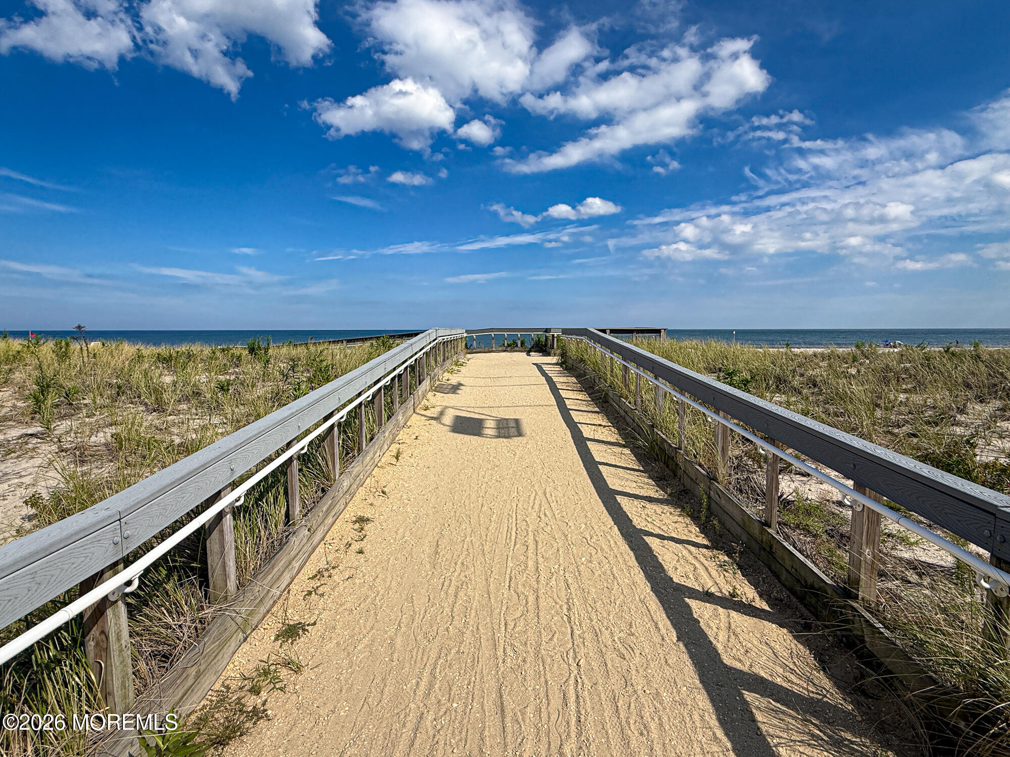 Wooden-railed sandy boardwalk through beach dunes leading to the ocean.