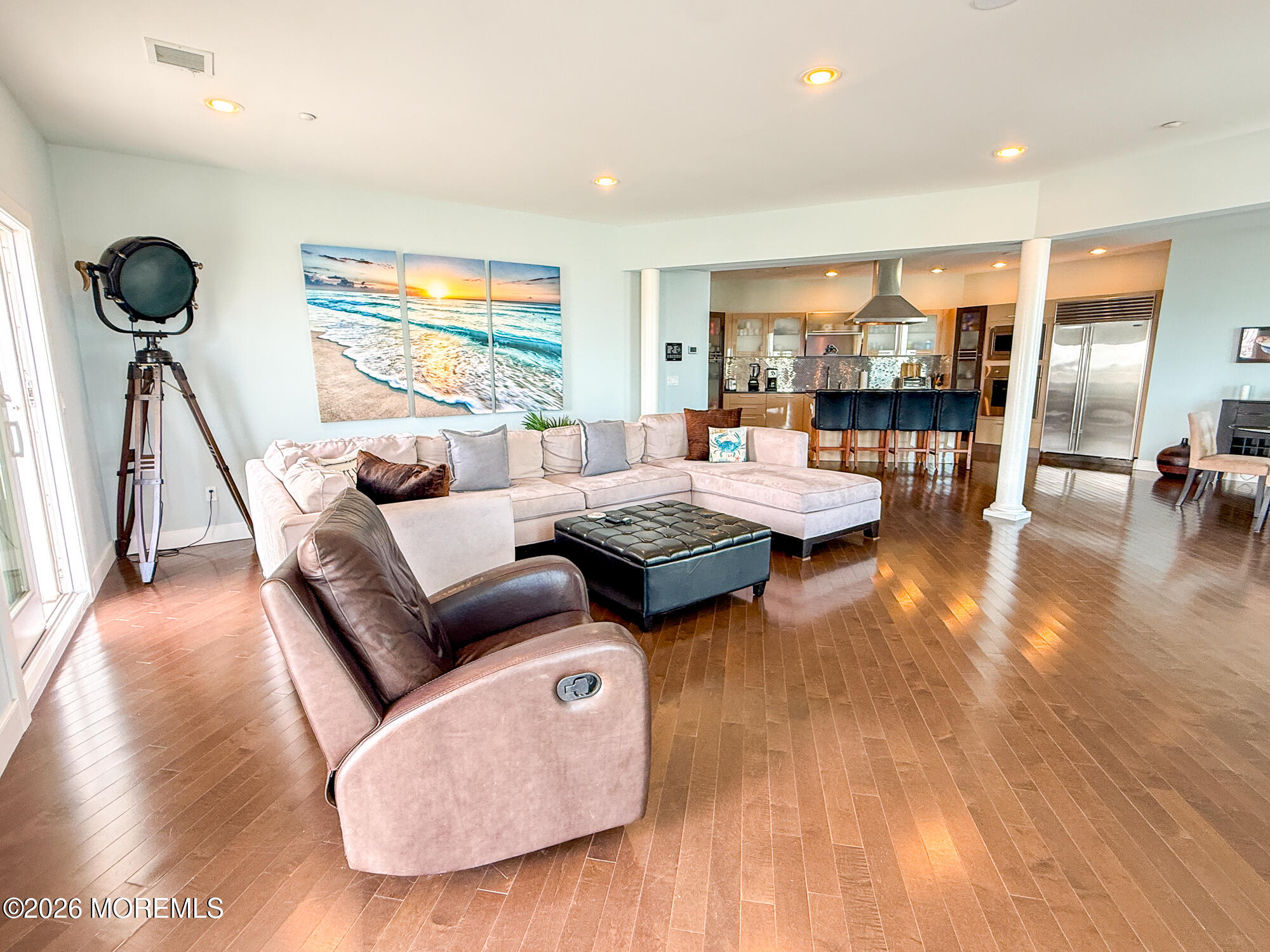 Living room with a cream sectional, leather recliner, hardwood floors, and an open kitchen beyond.