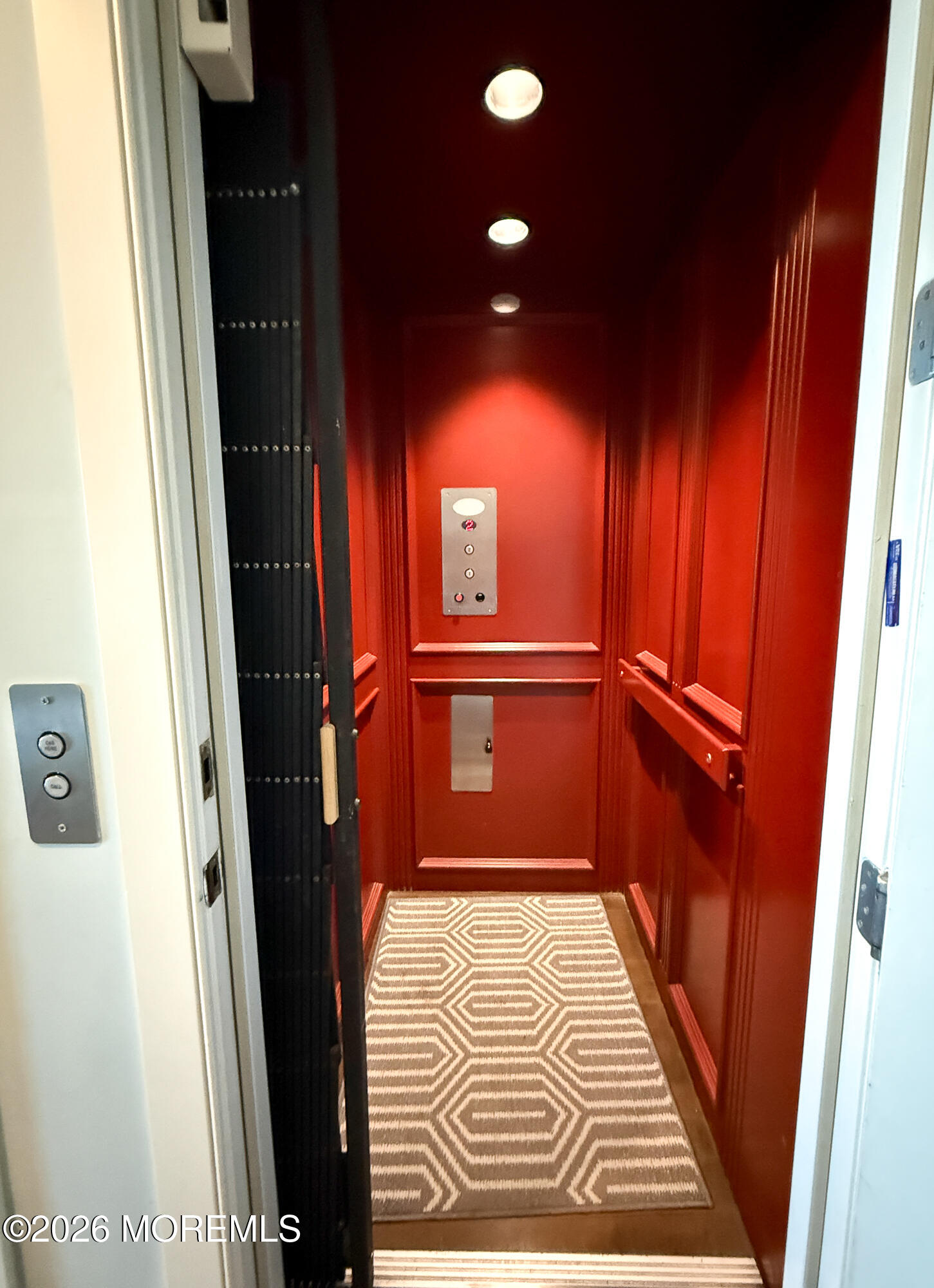 Red-paneled elevator with handrails and a beige geometric-patterned floor runner.