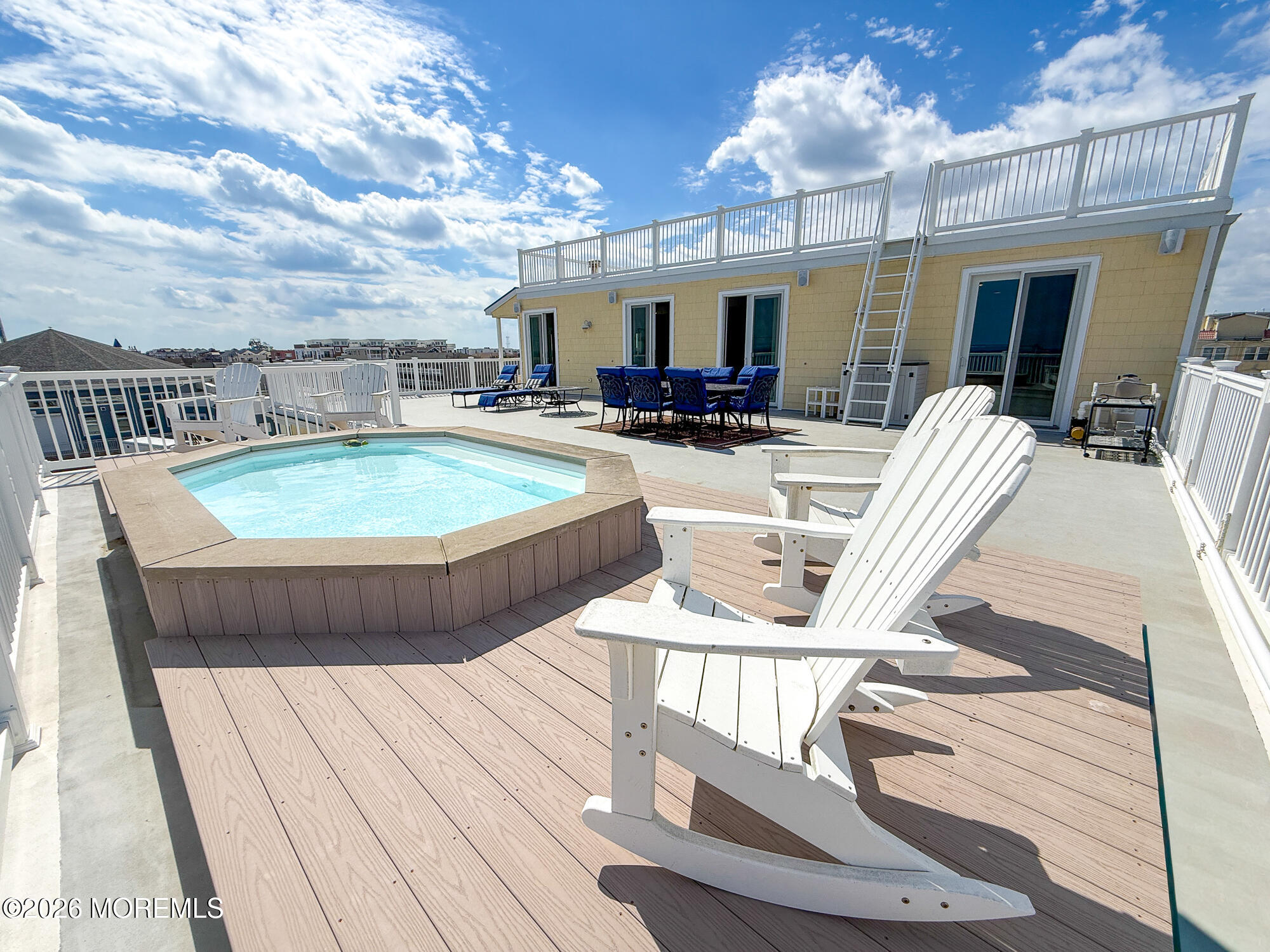 Rooftop deck with a raised hot tub, white Adirondack chairs, and outdoor dining area.