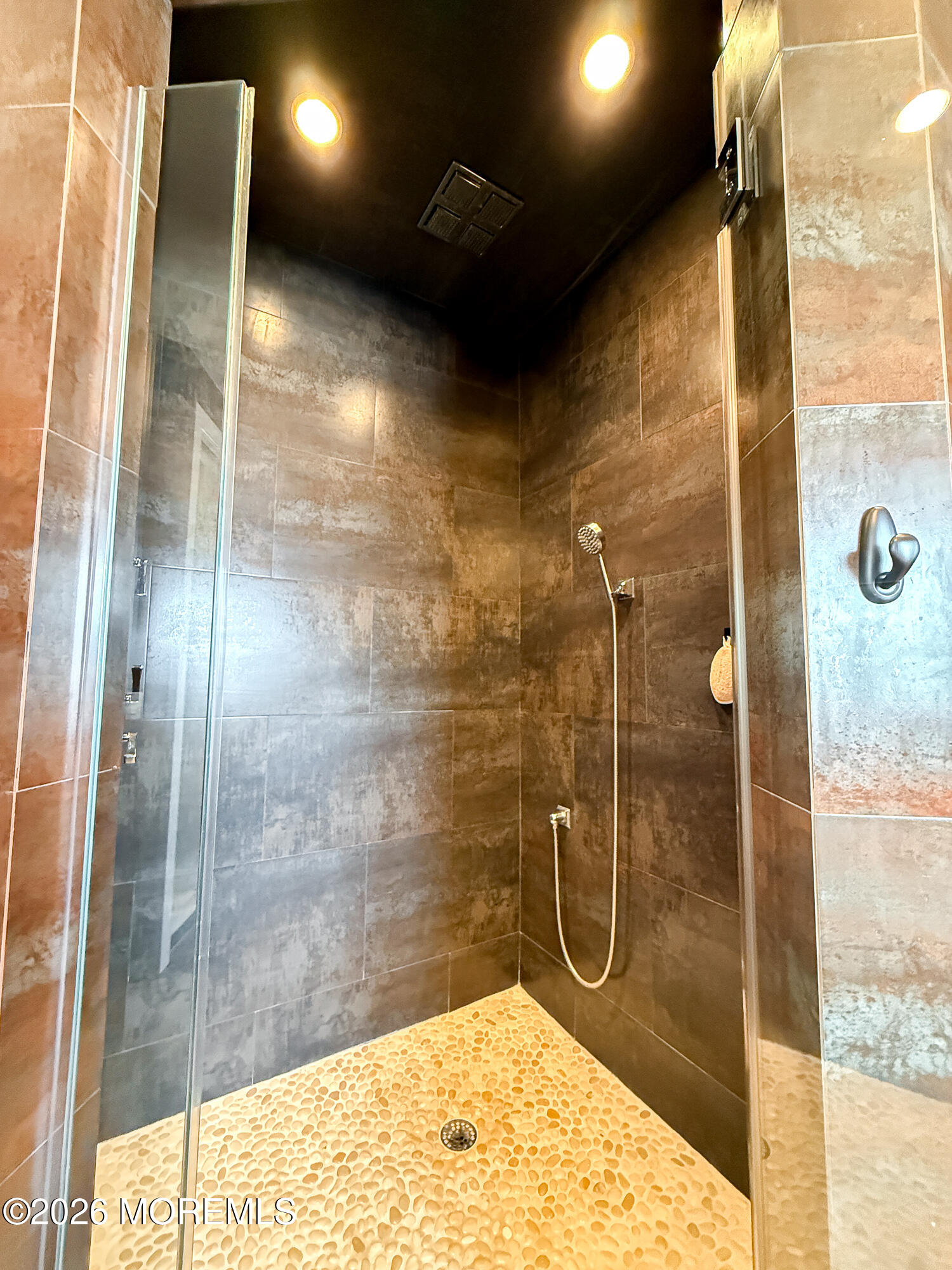 Walk-in shower with dark tile walls, a glass partition, and a light pebble-stone floor.