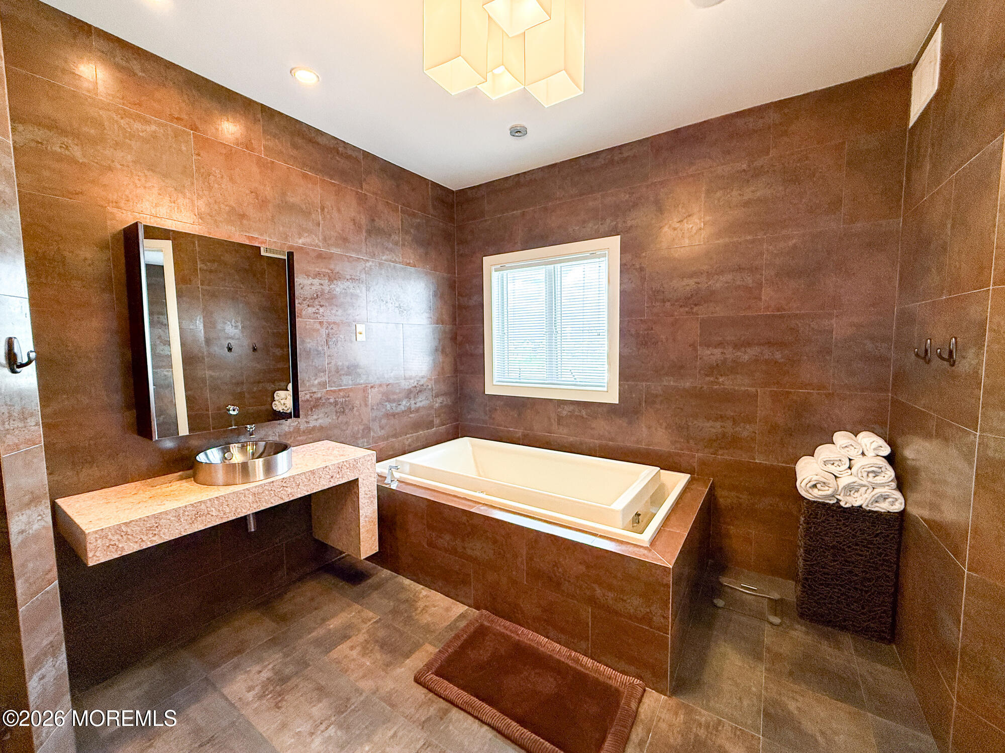 Bathroom with a built-in soaking tub, brown tile walls, and a floating vanity with vessel sink.