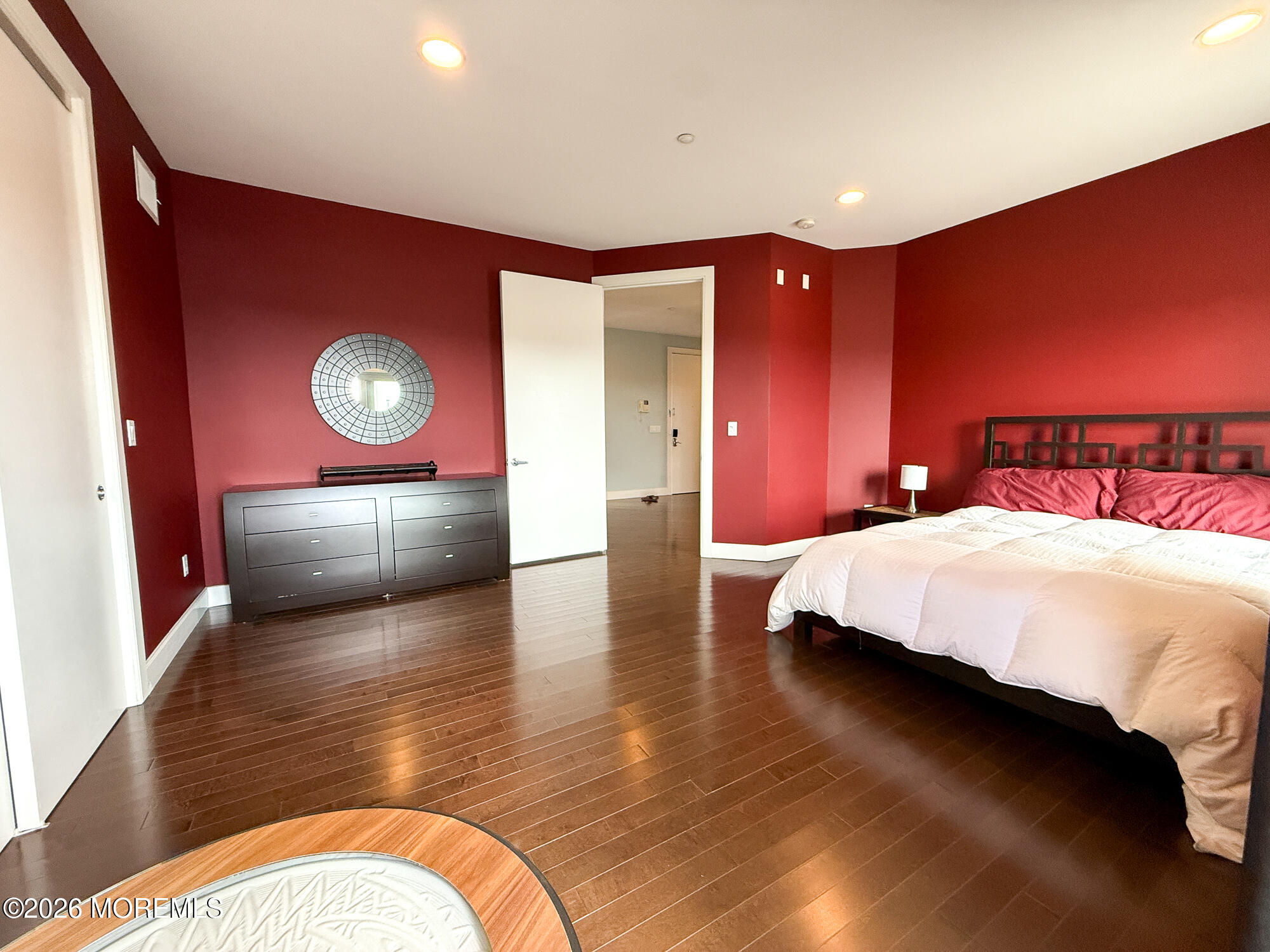Bedroom with deep red walls, dark hardwood floors, and a large bed with white bedding.