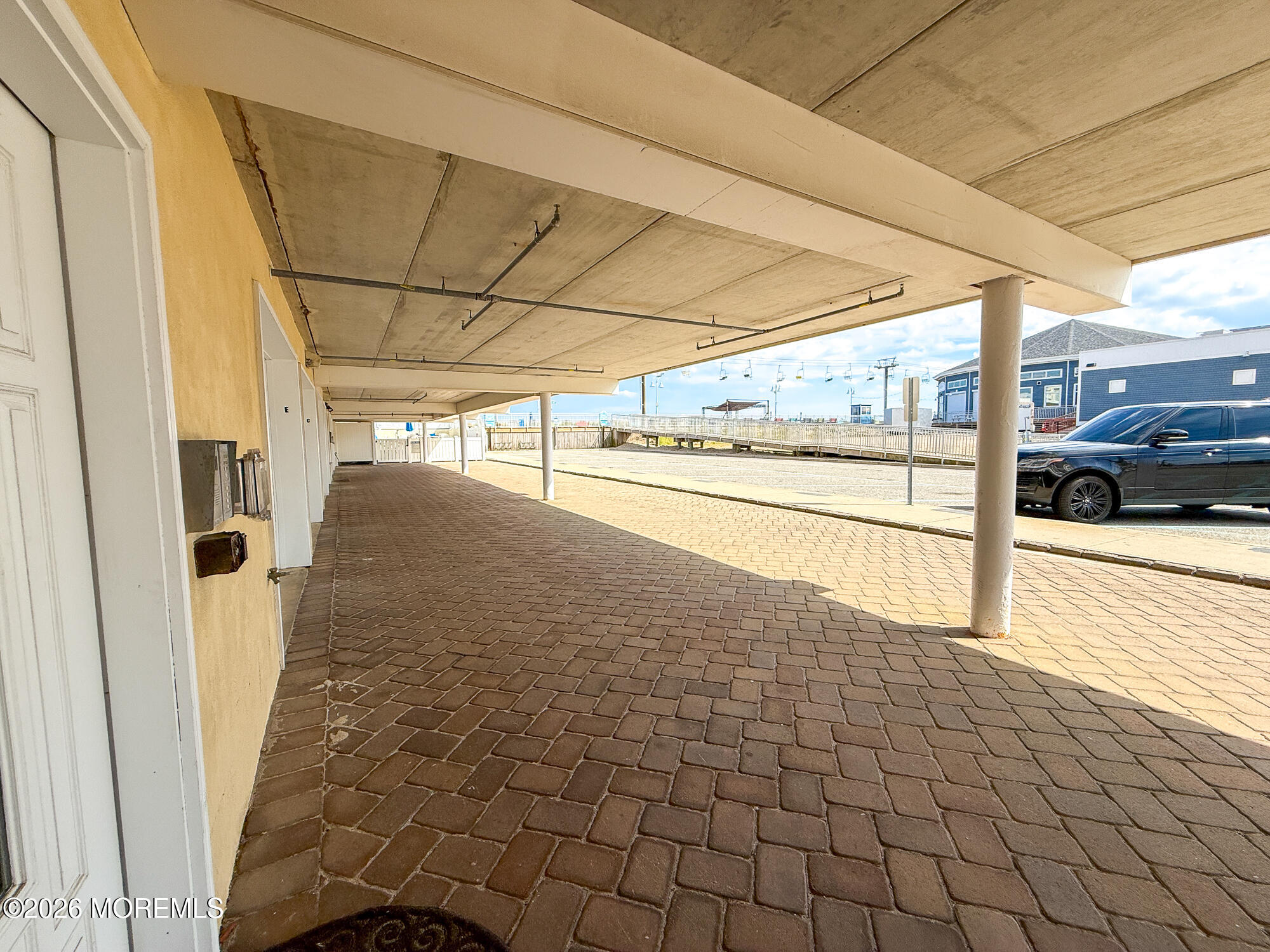 Covered brick-paved parking area beside the building, with support columns and a boardwalk beyond.
