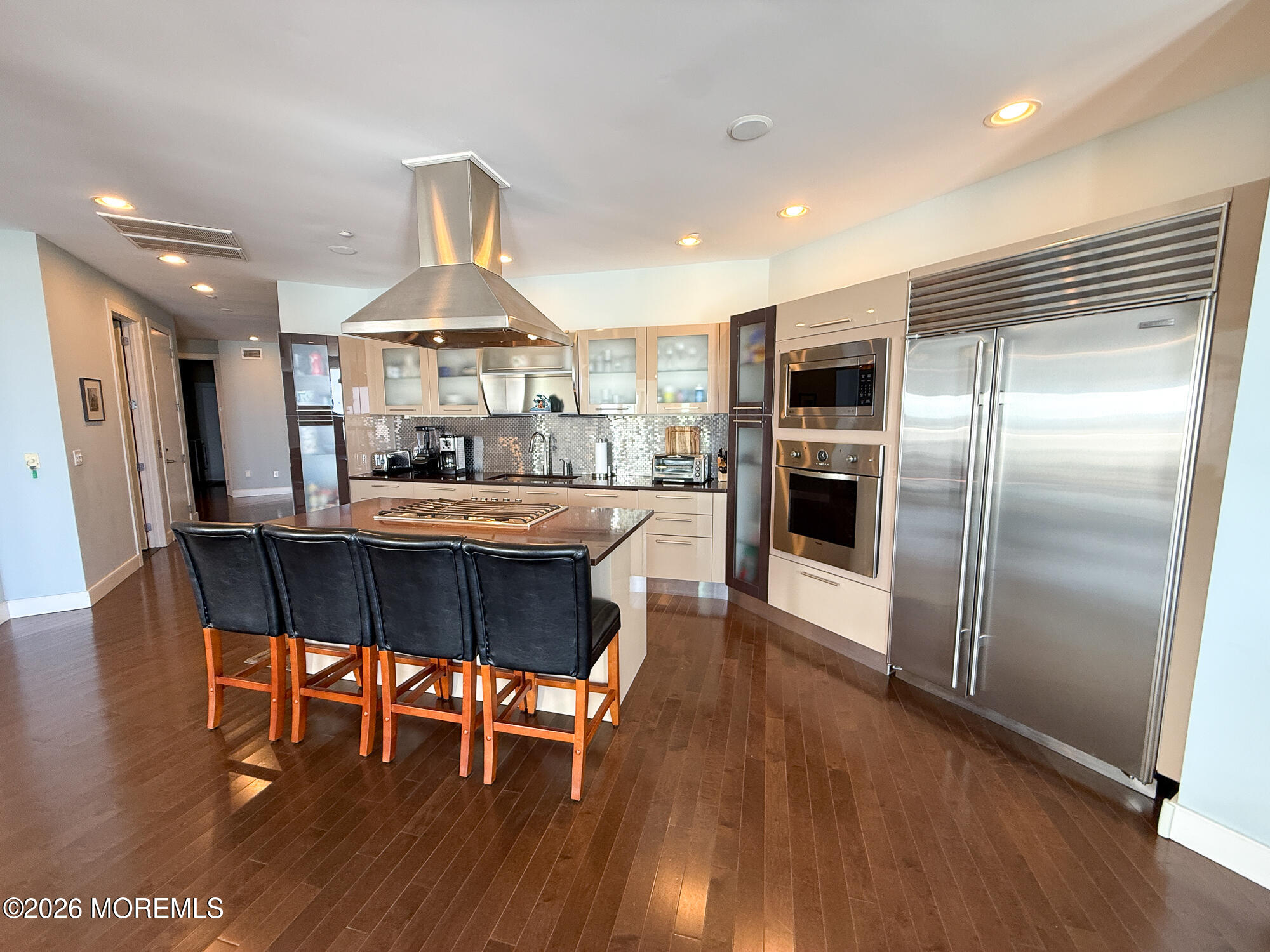Modern kitchen with a large island, four bar stools, and stainless steel appliances.