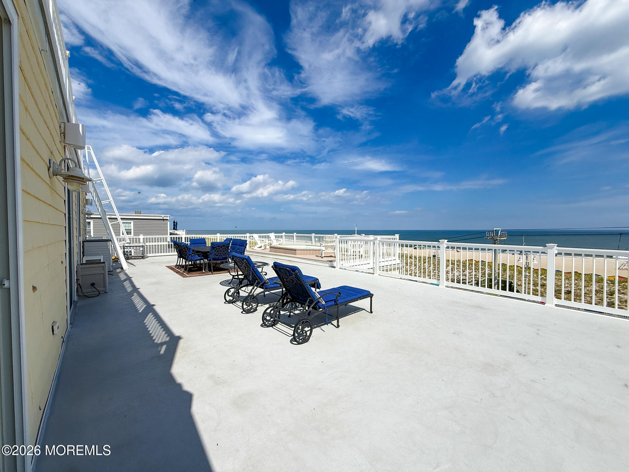 Seaside terrace with blue lounge chairs, white railings, and views across the ocean.