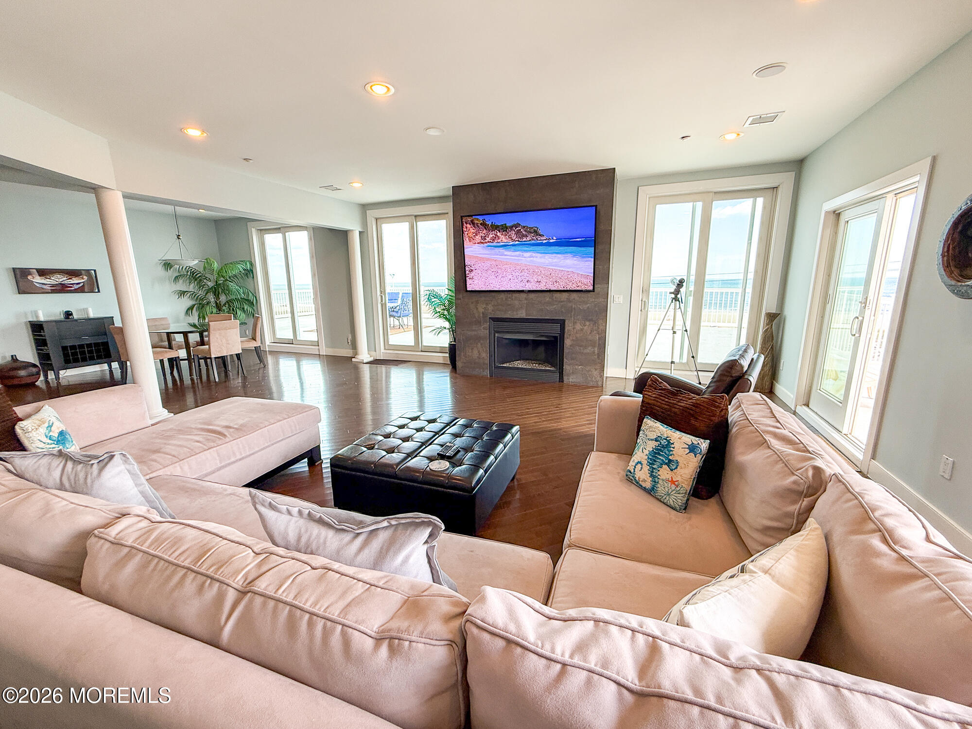 Living room with a fireplace, pale sectional sofas, and ocean views through sliding glass doors.