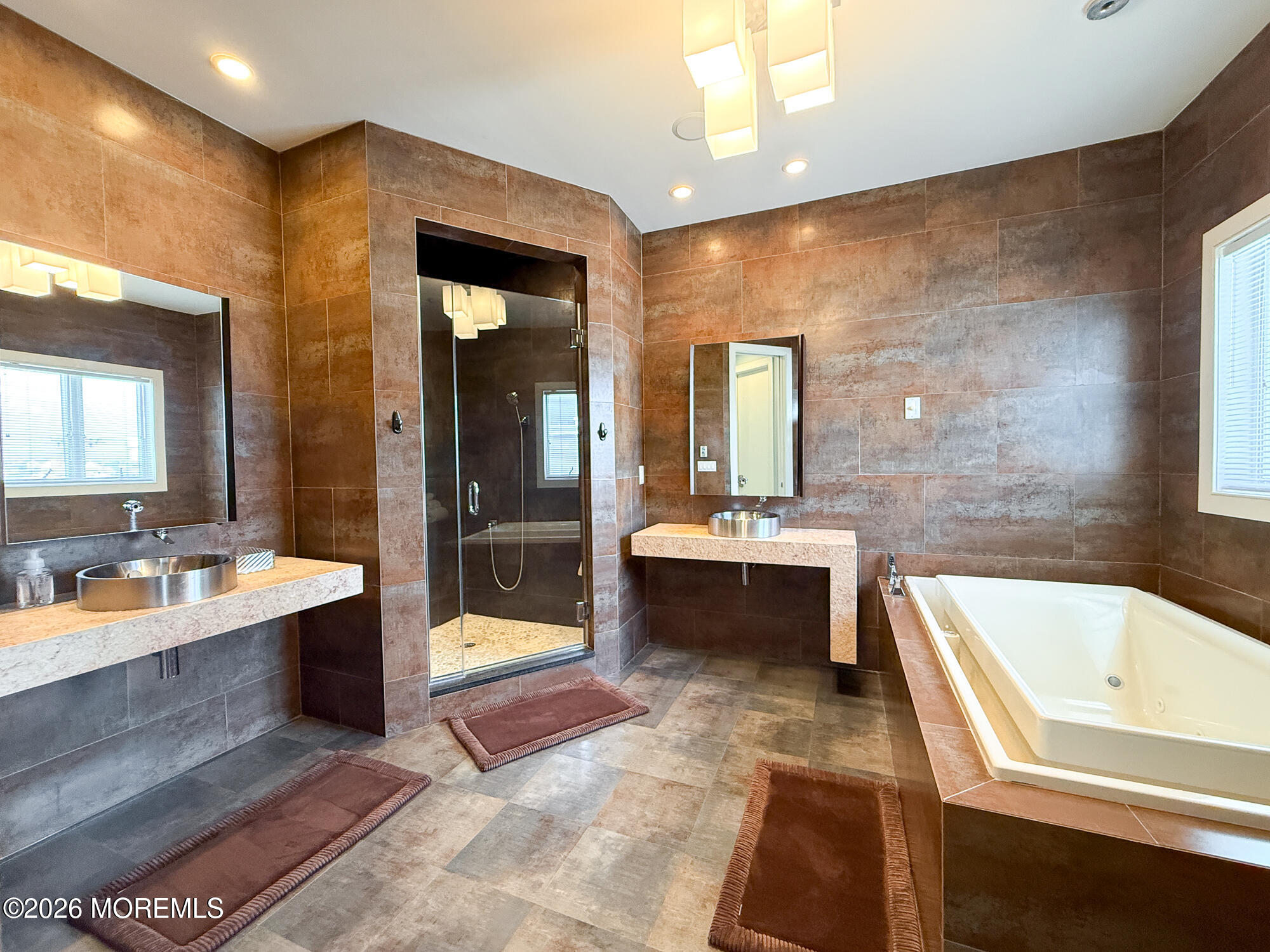 Modern tiled bathroom with a glass shower, soaking tub, and two vessel-sink vanities.