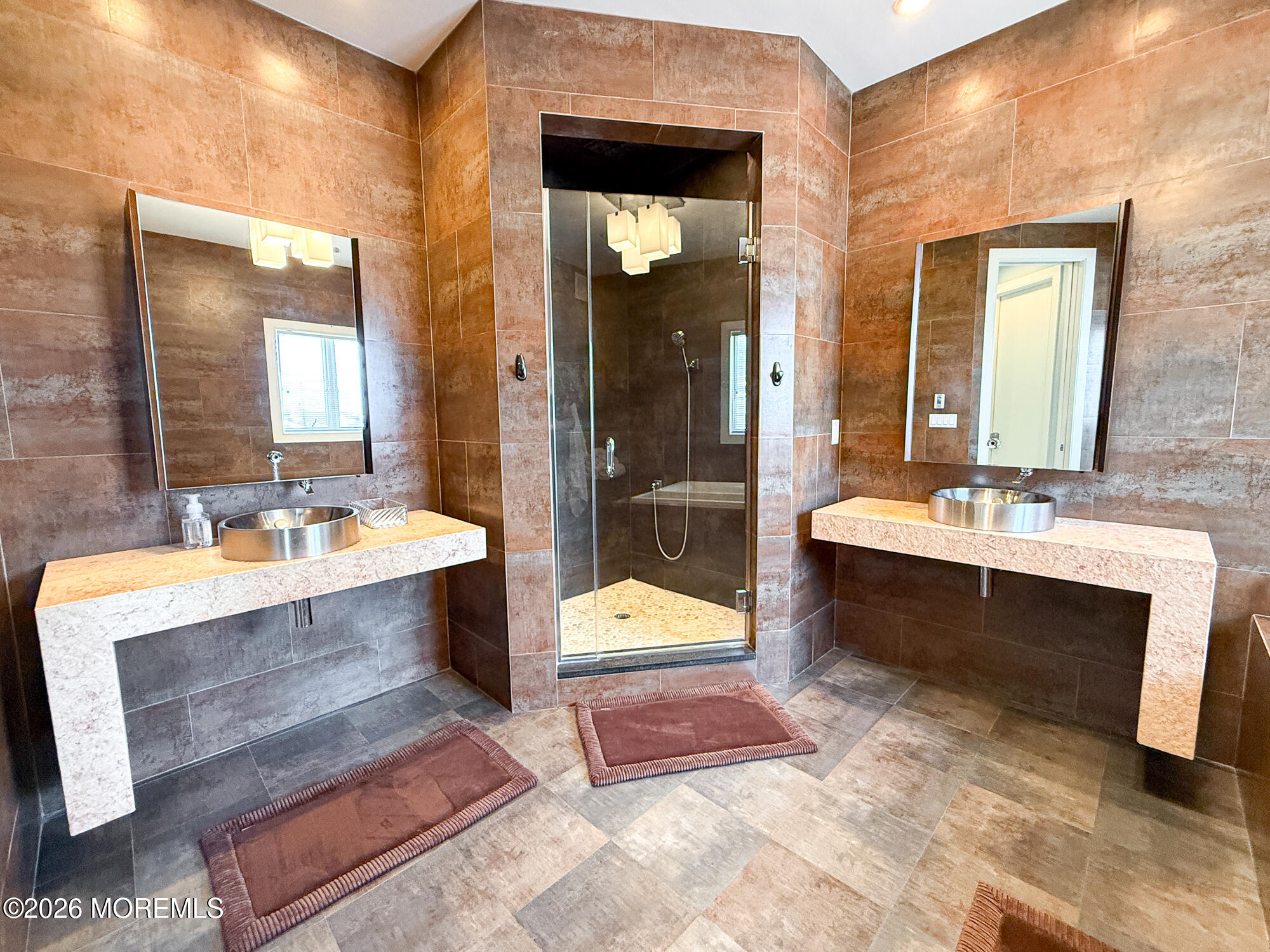 Bathroom with dual stone vanities and a central glass-enclosed shower.