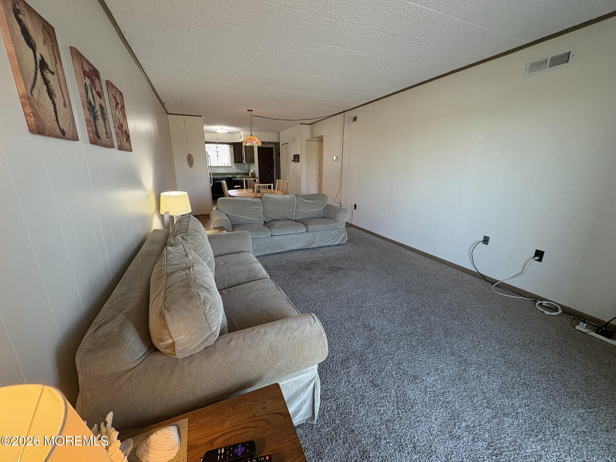 Living room with gray sofas and carpet, looking toward the dining area and kitchen.