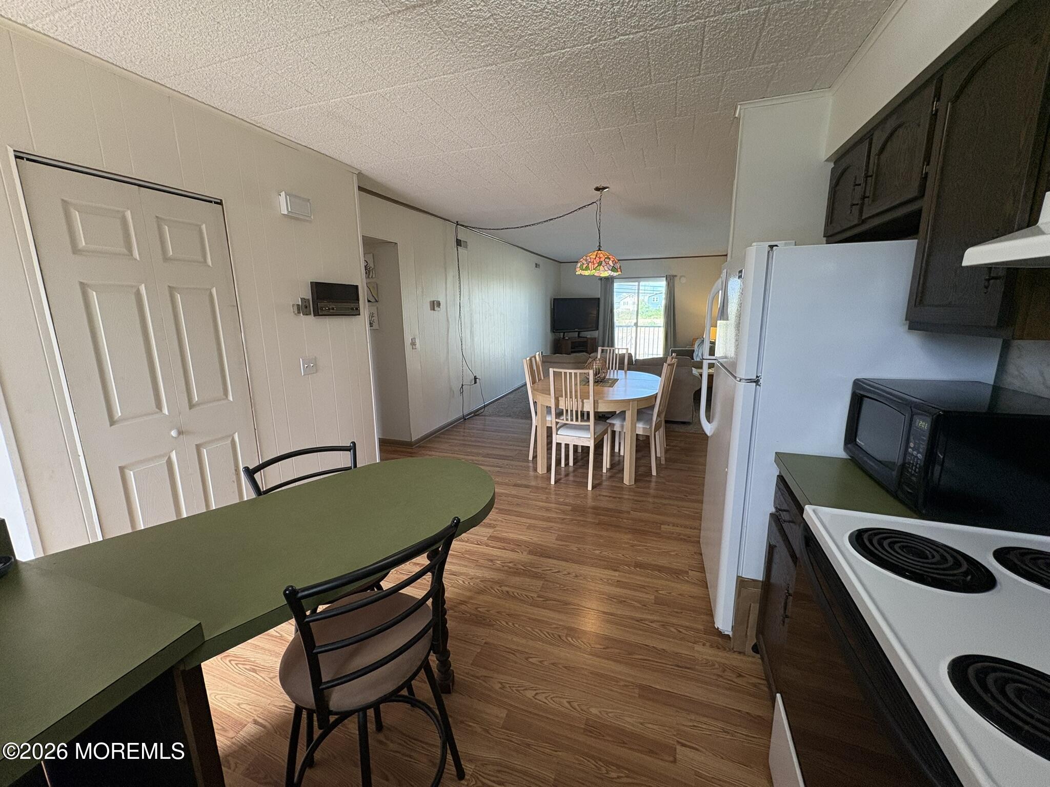 Open-plan kitchen and dining area with dark cabinets, wood-look floors, and a stained-glass pendant.