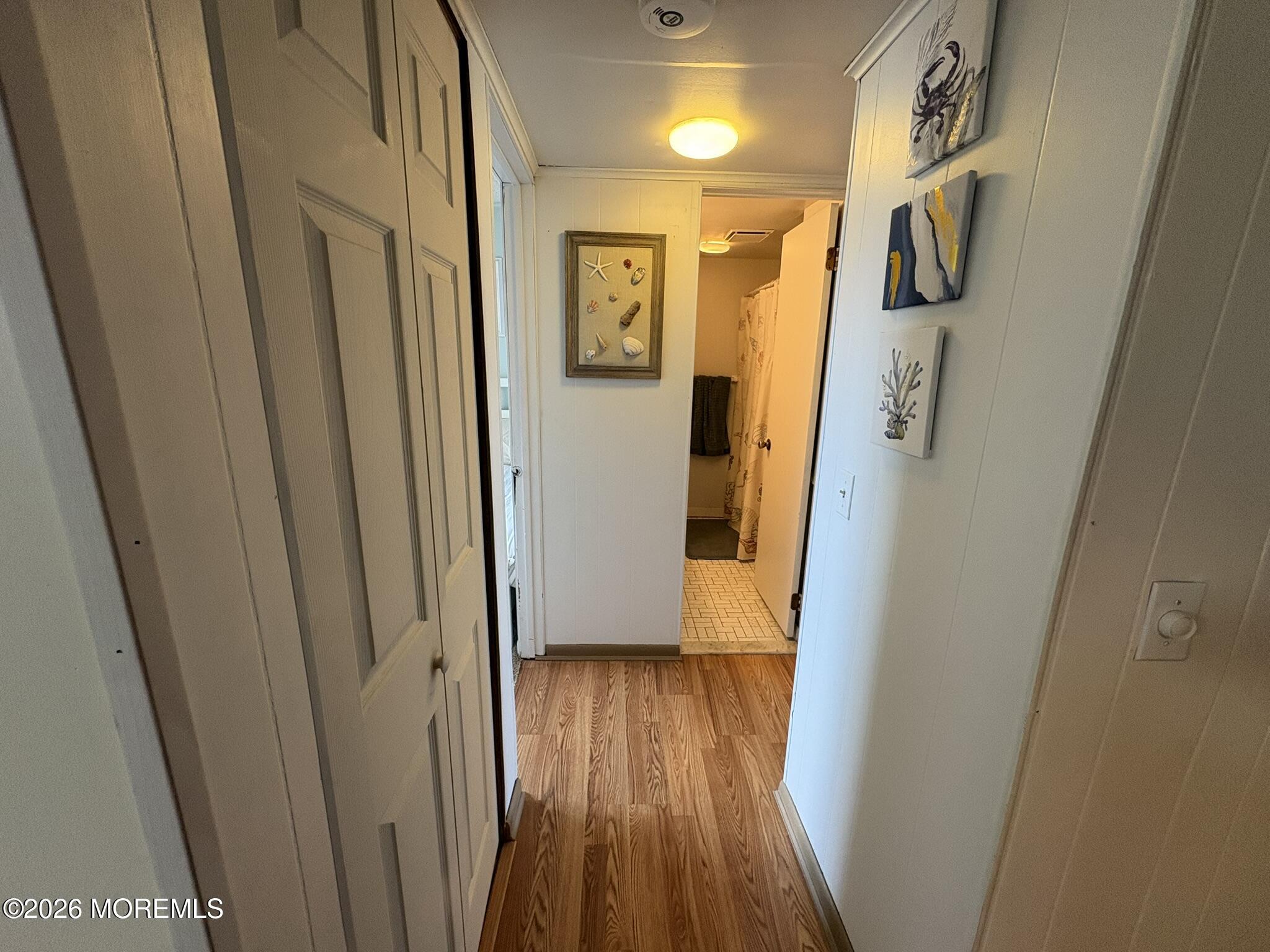 Hallway with wood-look flooring, coastal wall art, and an open doorway to a bathroom.