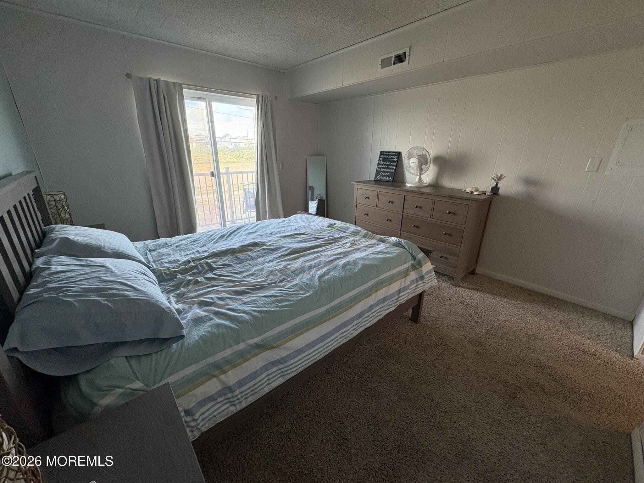 Bedroom with blue striped bedding, a wooden dresser, and sliding glass doors to a balcony.