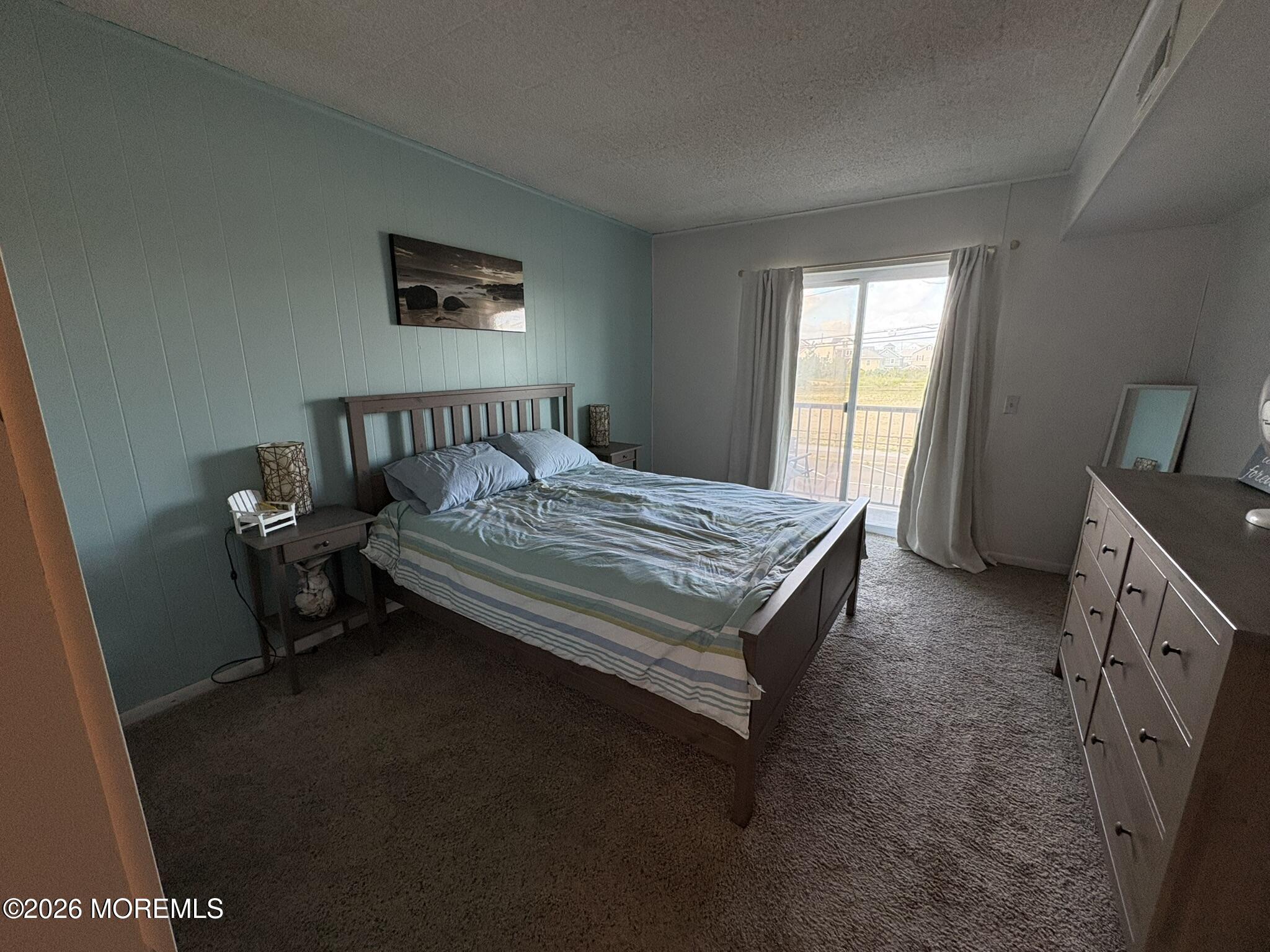Bedroom with striped blue bedding, a blue paneled wall, and a sliding glass door to the balcony.