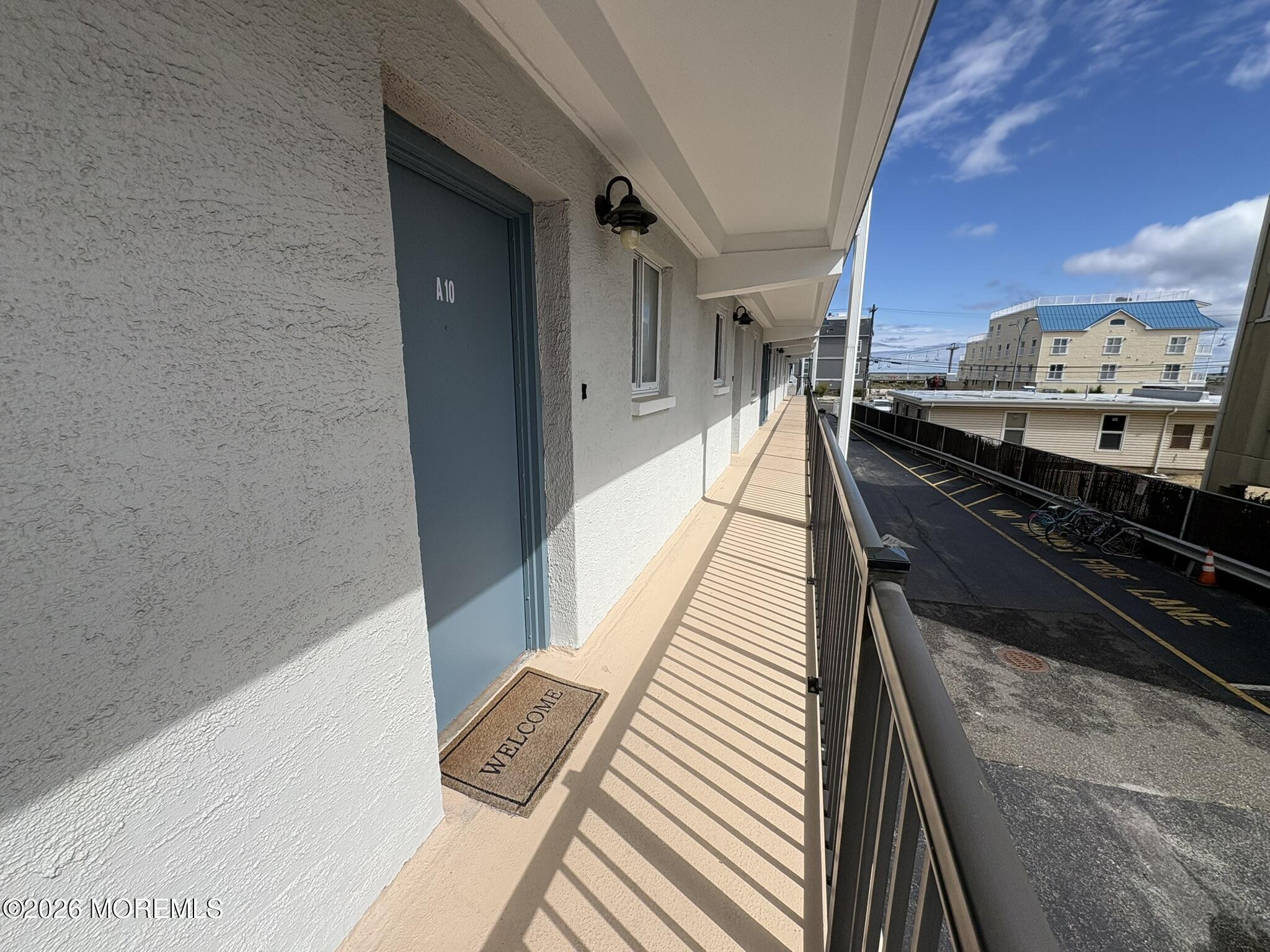 Covered walkway to unit A10, with a blue door, welcome mat, and railing overlooking the parking area.