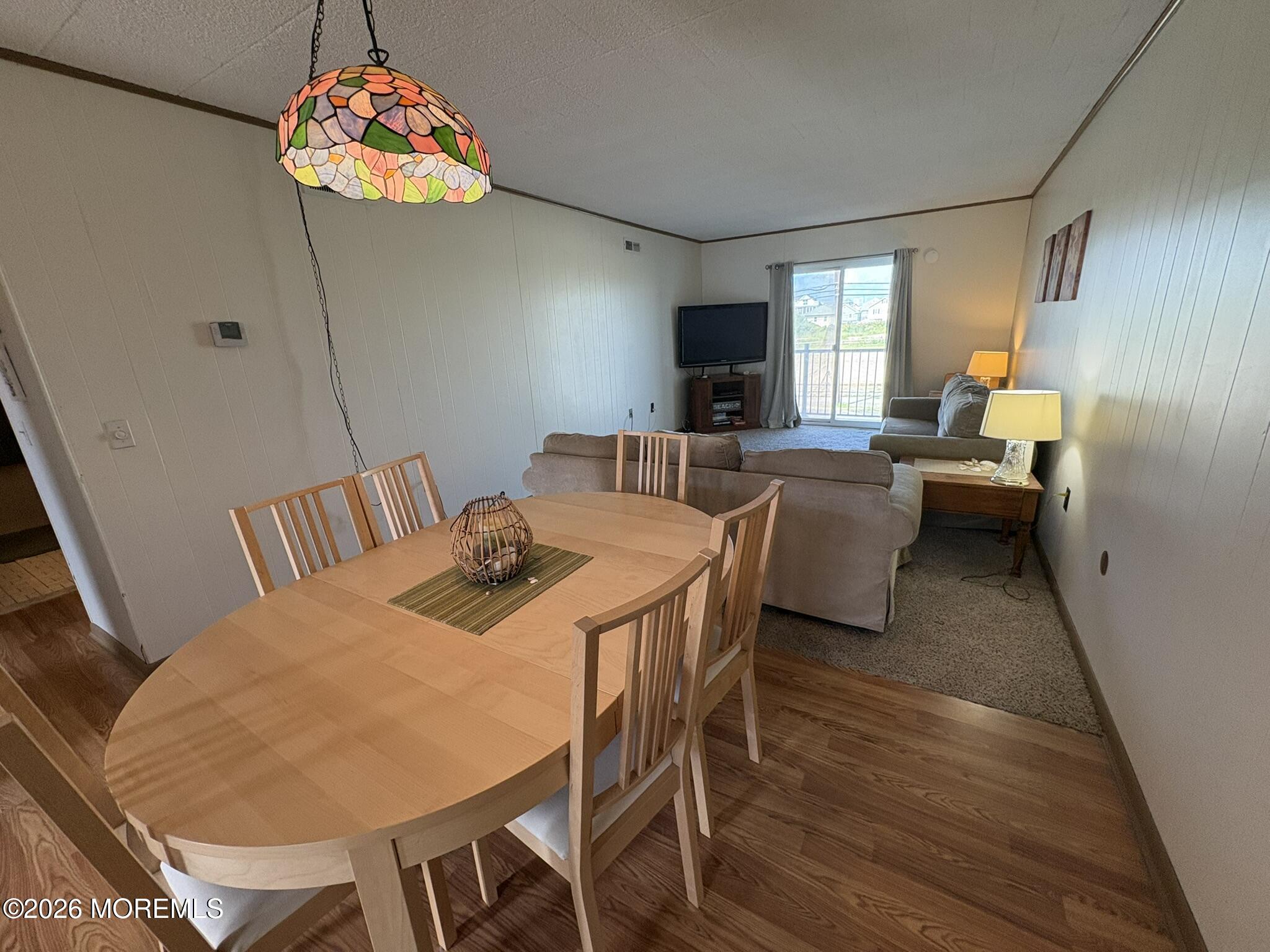 Open-plan dining and living room with a round wood table, beige sofas, and a balcony door.