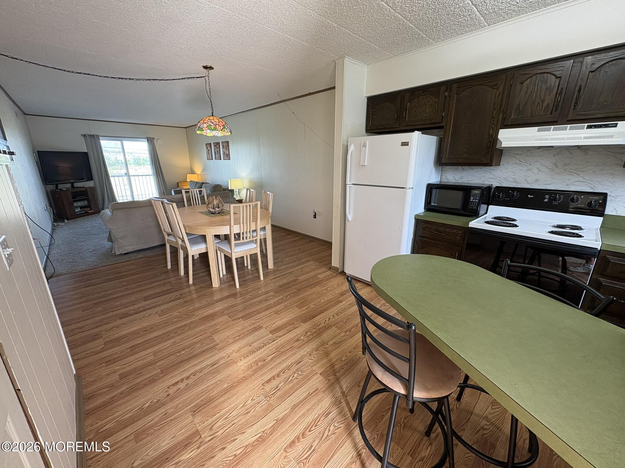 Open-plan kitchen and living area with dark cabinets, white appliances, and a green peninsula.