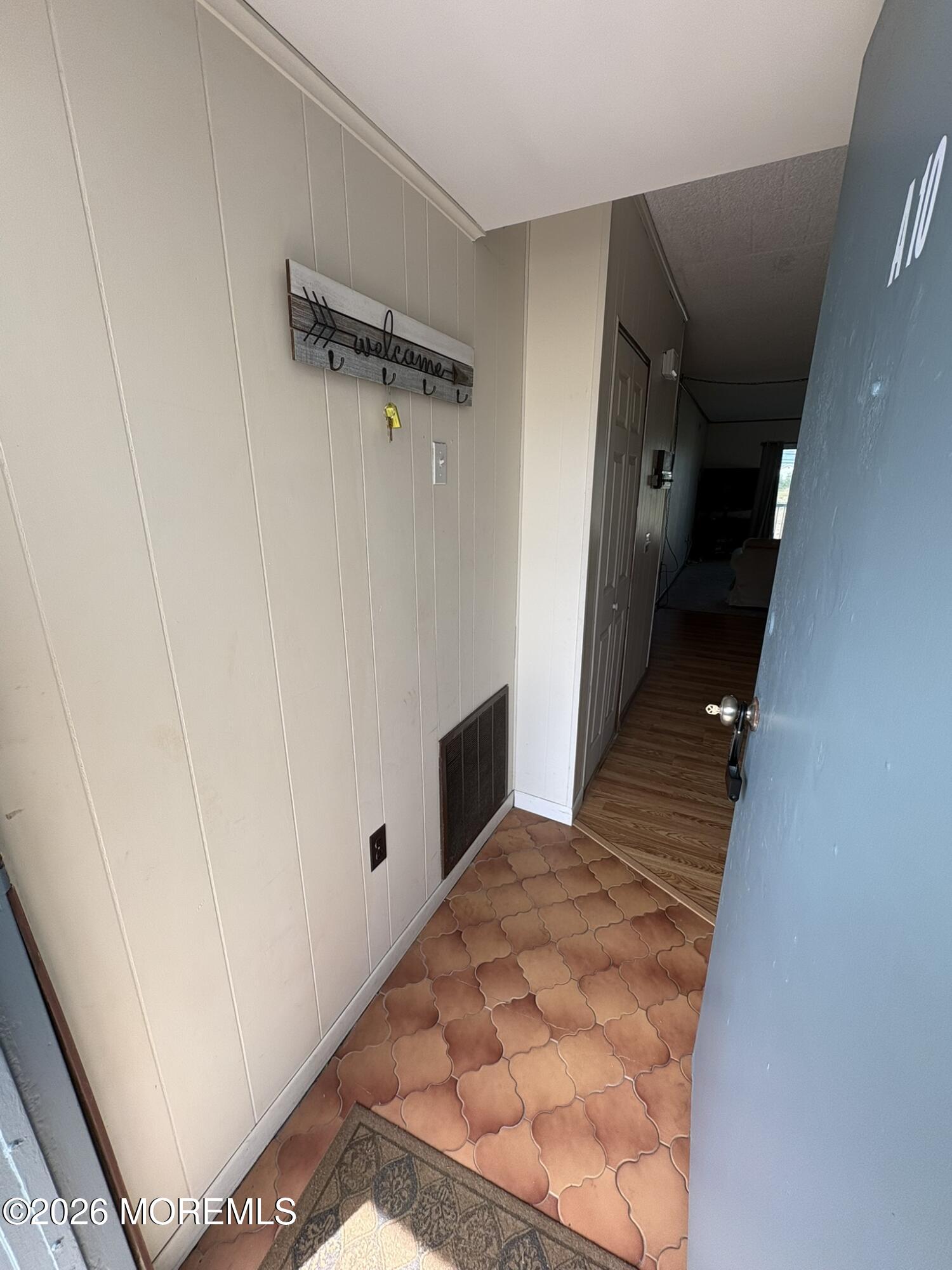 Entry hallway with patterned terracotta tile, cream paneled walls, and a blue door.