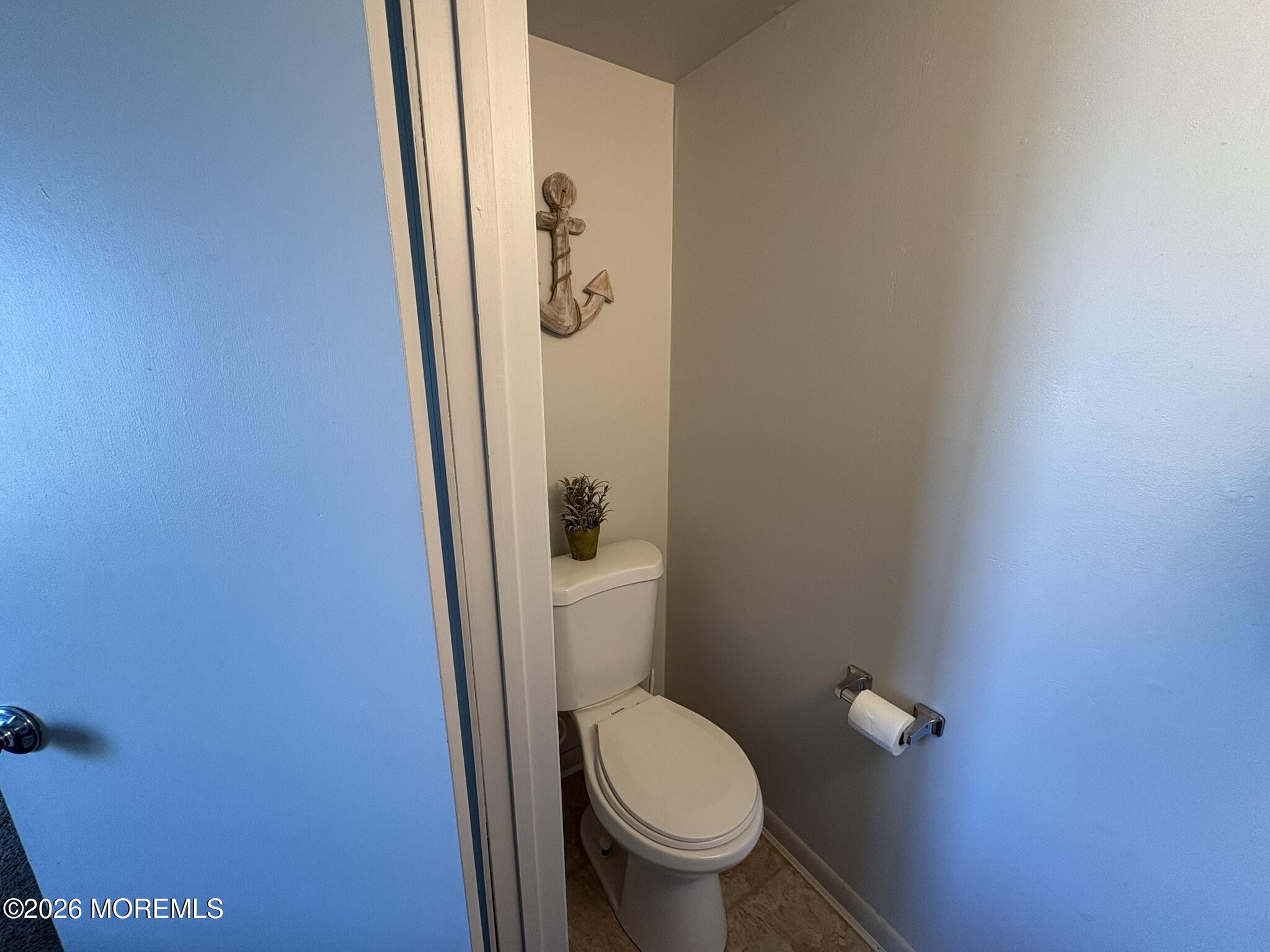 Small half bathroom with a toilet, nautical anchor wall decor, and potted plant.
