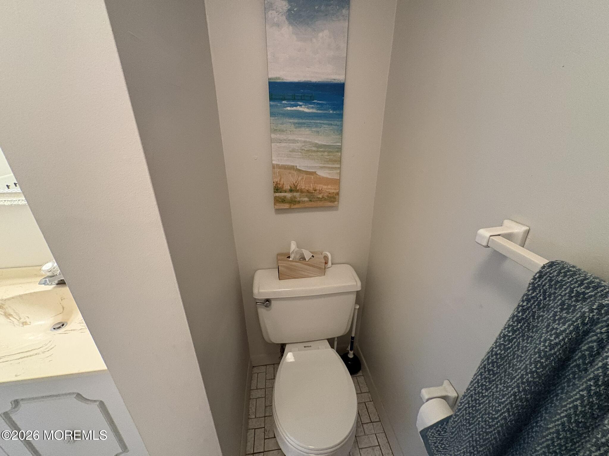 Compact bathroom with a white toilet beneath beach artwork and a blue towel on the wall.