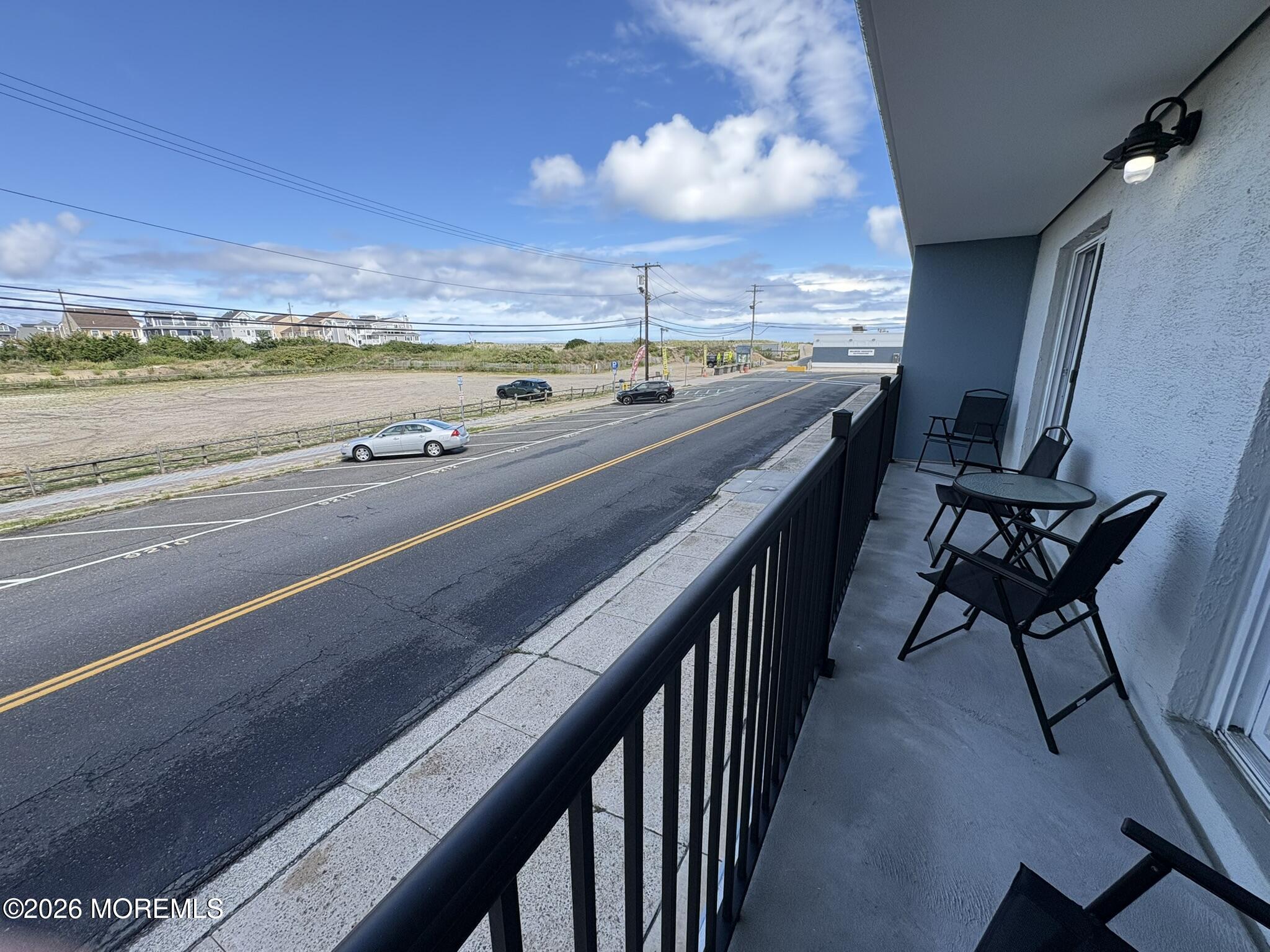 Furnished balcony overlooking a road and dunes, with a distant ocean view.