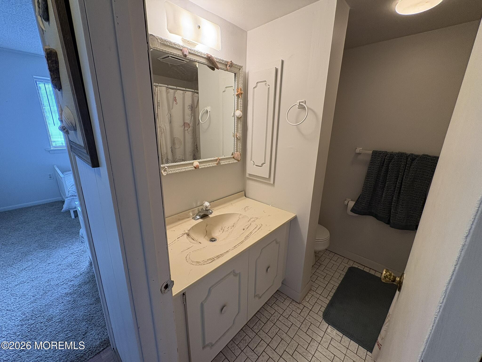Bathroom with a cream vanity, decorative mirror, tiled floor, and dark towels beside the toilet.
