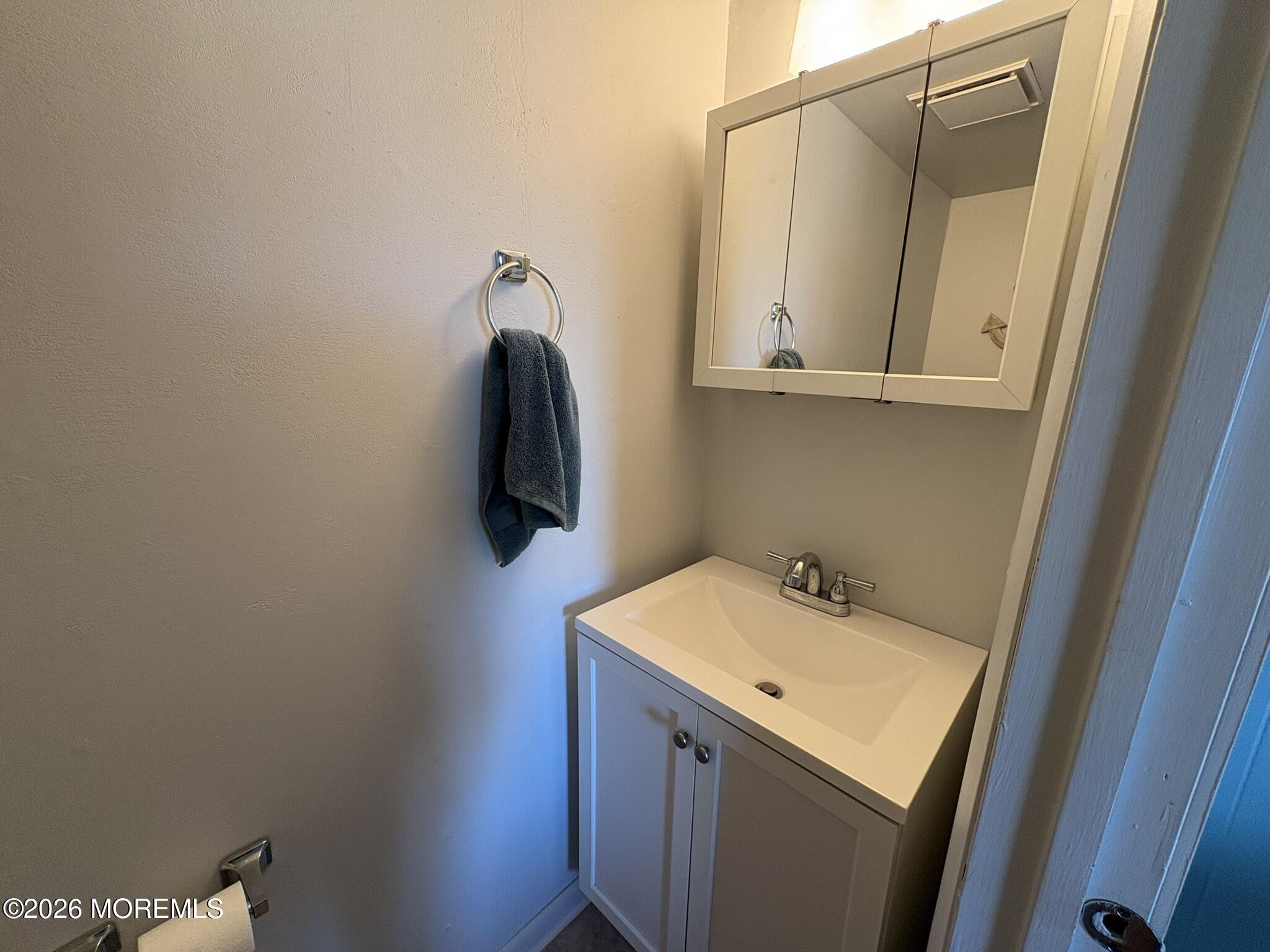 Bathroom vanity with a mirrored medicine cabinet and dark towel on a wall ring.