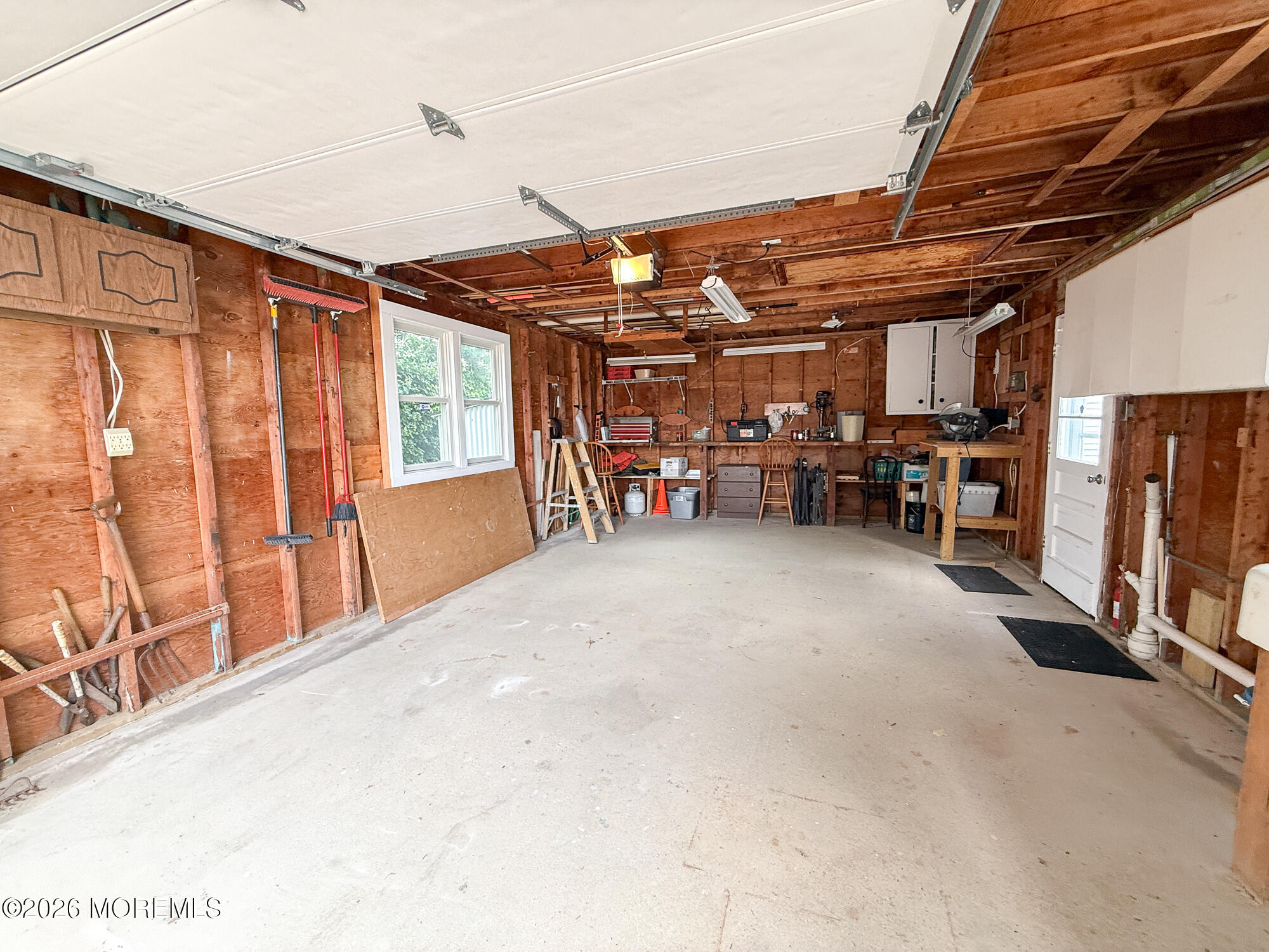 Garage with exposed wood walls, concrete floor, and workbenches and tools along the back wall.