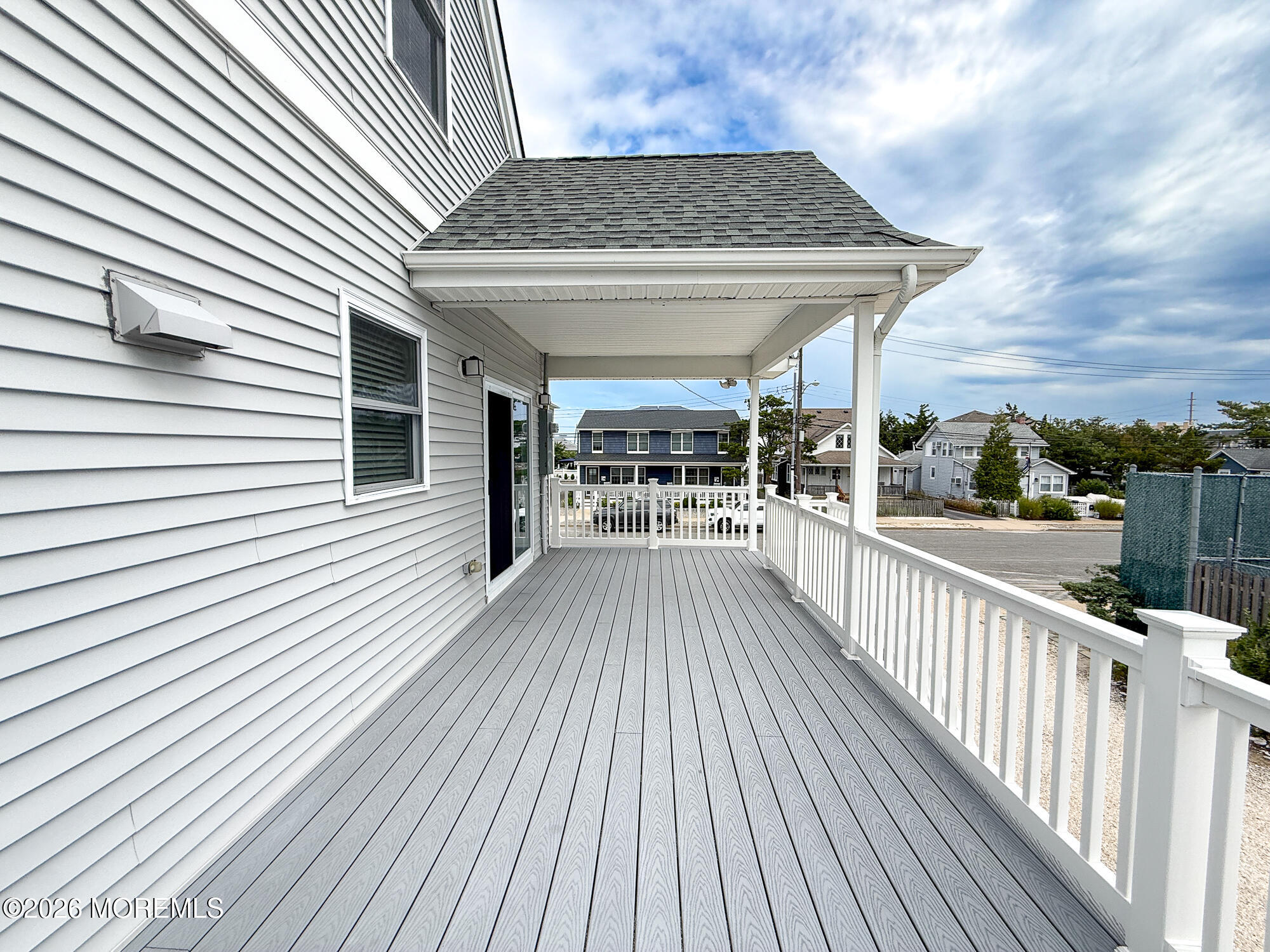 Covered gray deck with white railings alongside a white-sided house.