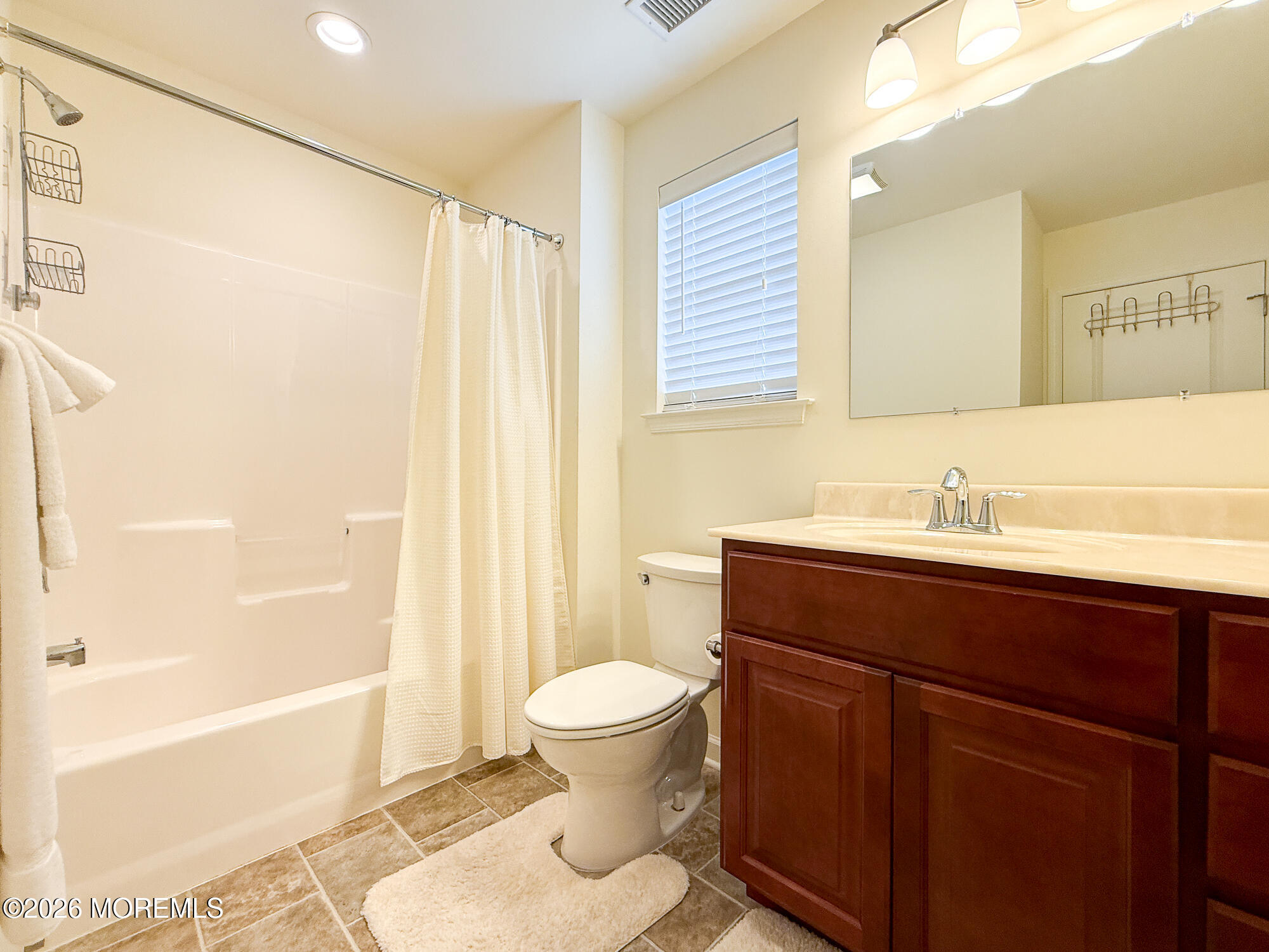 Bathroom with a white tub and shower, toilet, and dark wood vanity beneath a wide mirror.