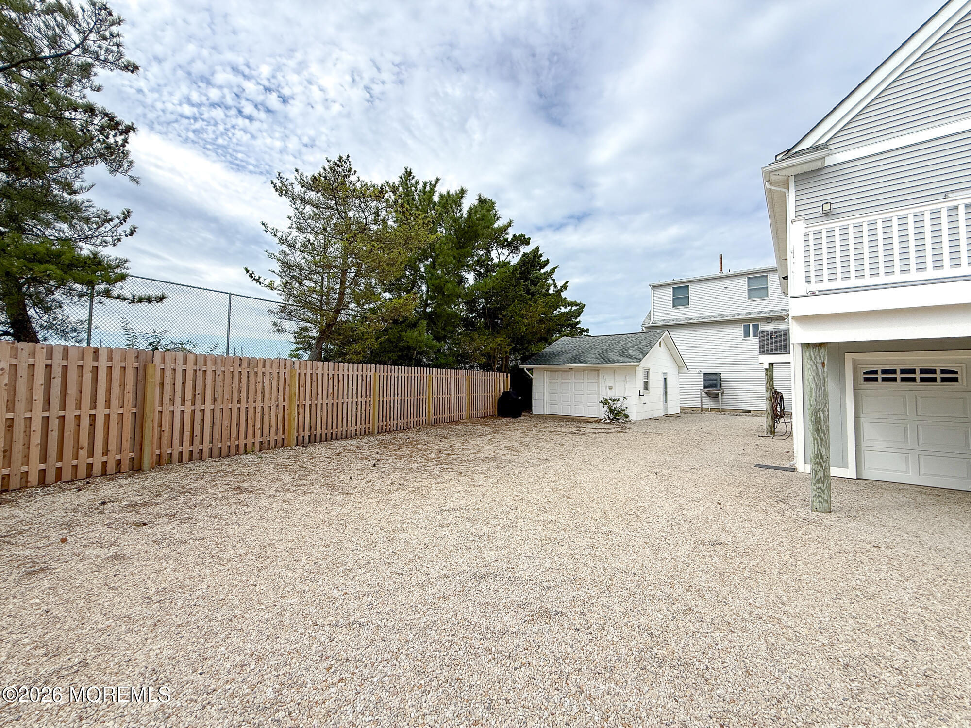 Gravel yard with a wooden fence, detached shed, and raised house with garage.