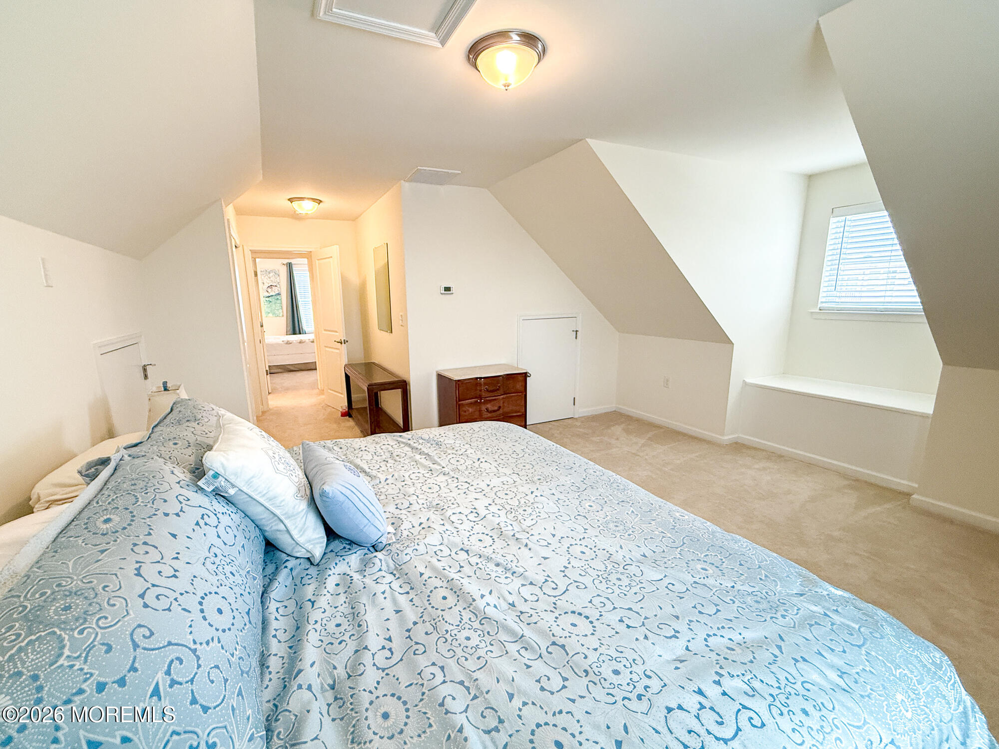 Upstairs bedroom with sloped ceilings, a skylight, beige carpet, and blue-and-white patterned bedding.