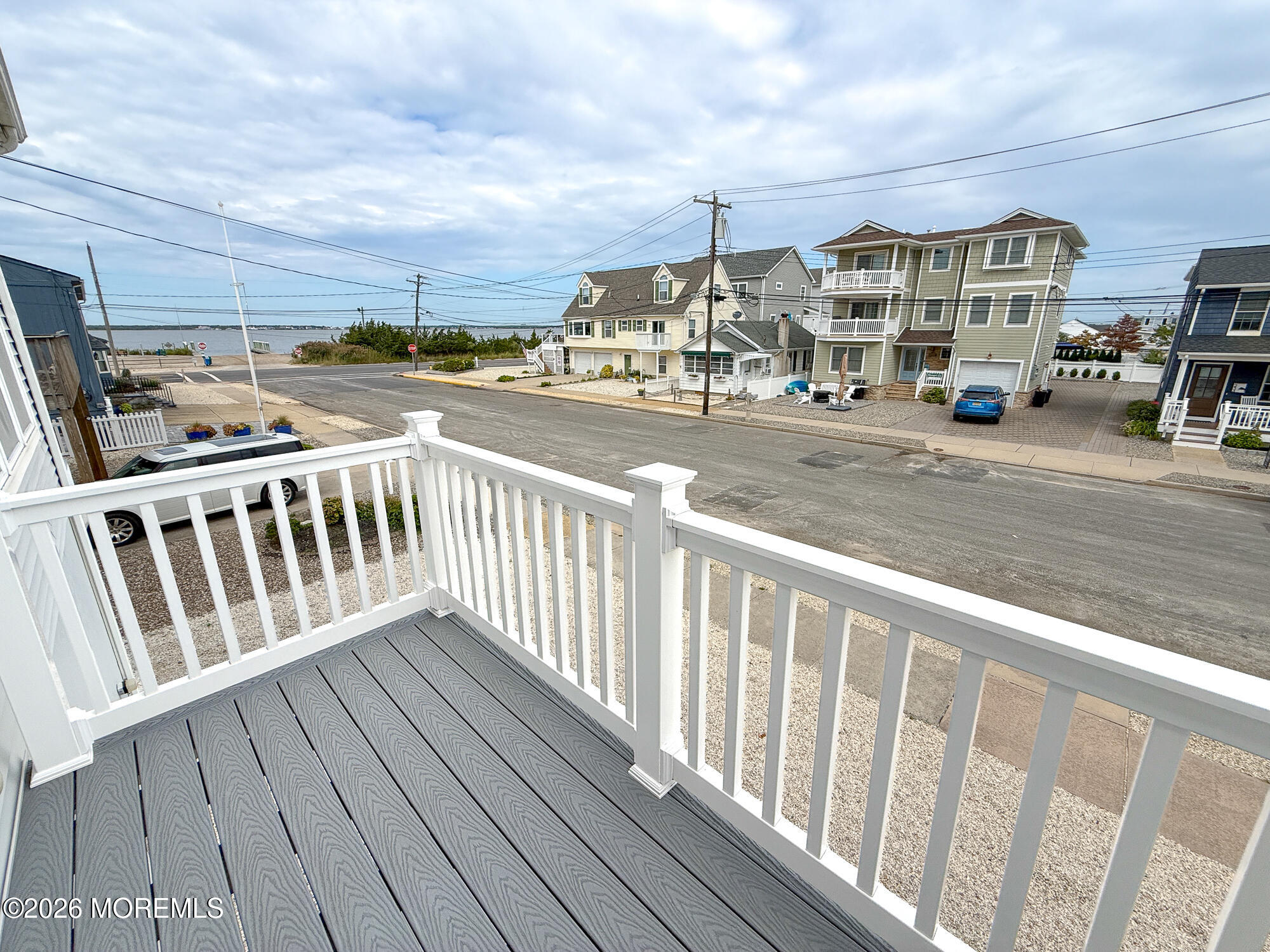 Gray deck with white railing overlooks a coastal street and water.