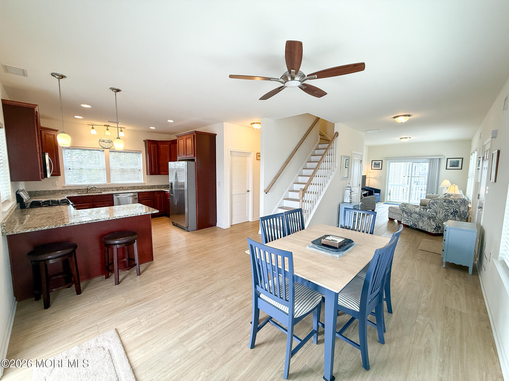 Open-plan kitchen and dining area with granite counters, blue chairs, and a staircase leading toward the living room.