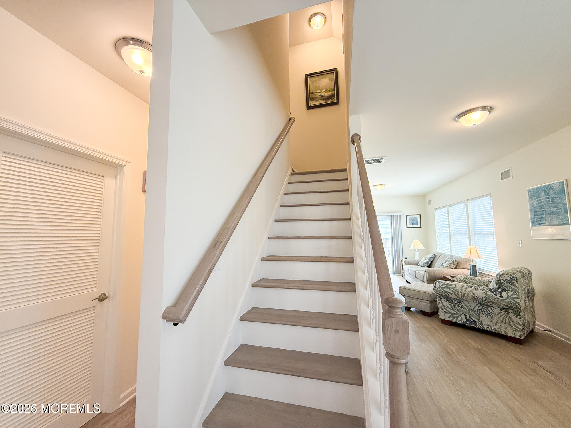 Staircase with wood treads beside a furnished living room with large windows.