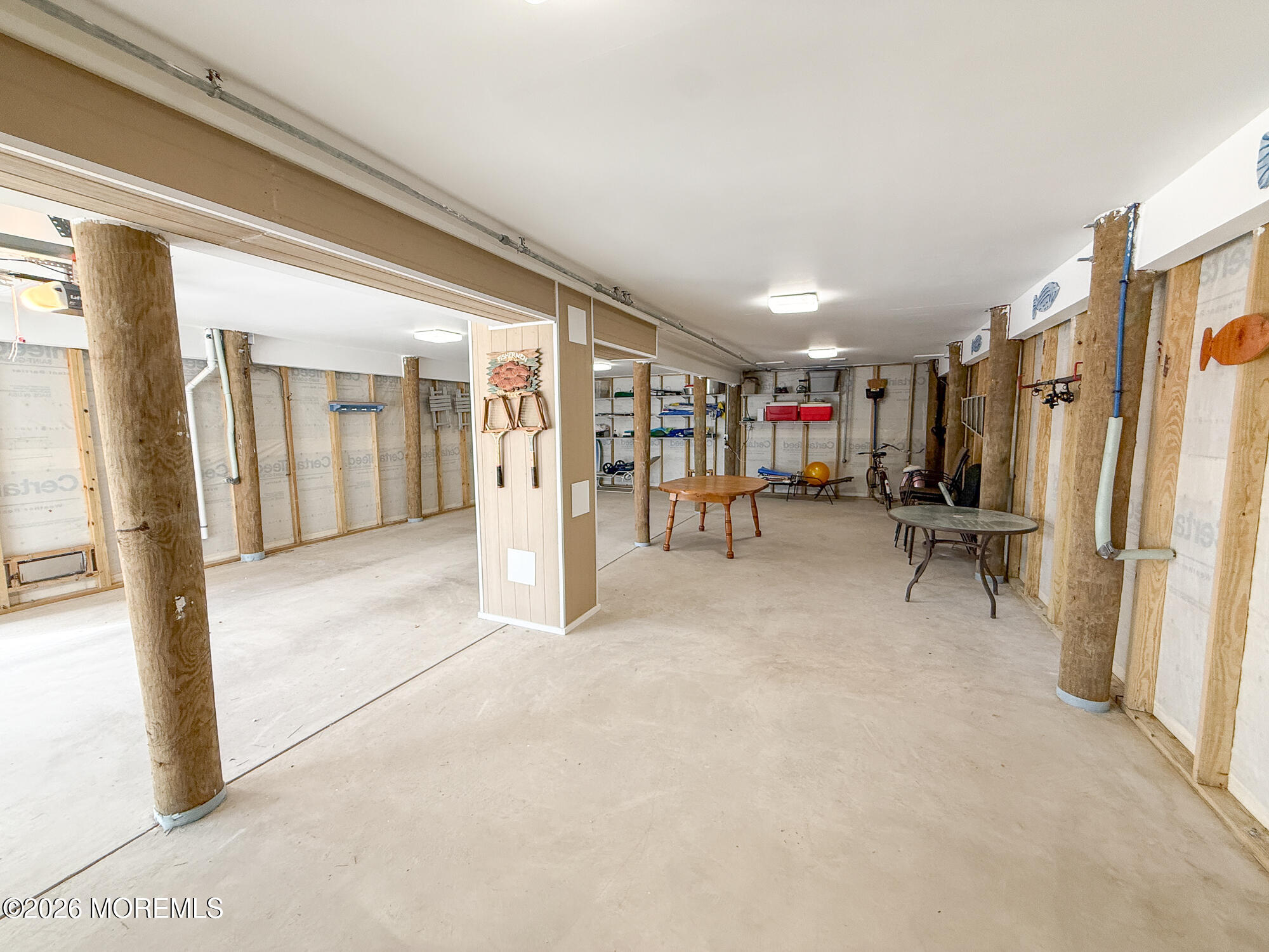 Unfinished basement with exposed framing, wood support posts, and scattered tables and chairs.