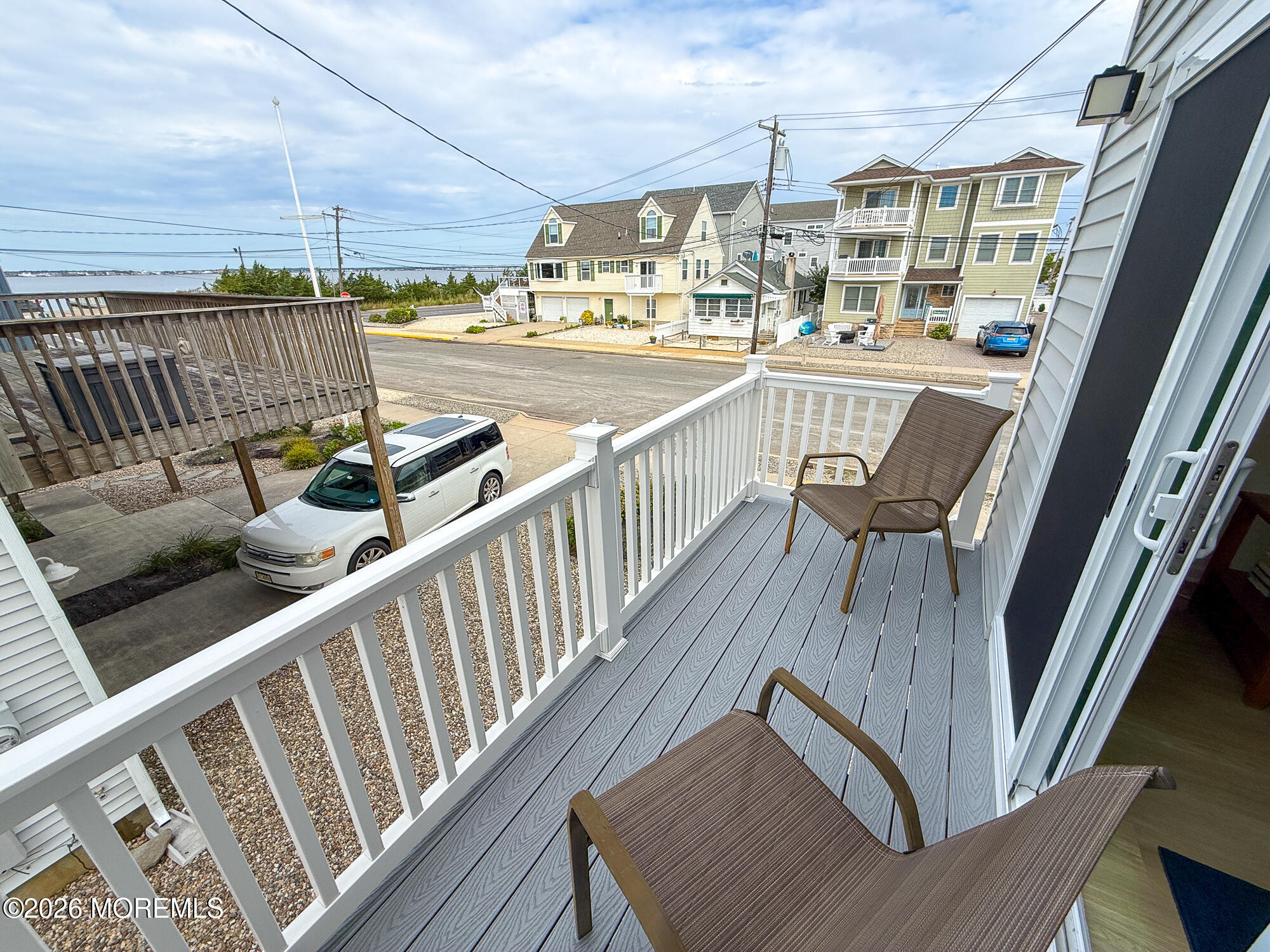 Furnished balcony with white railings overlooking neighboring homes and distant water.