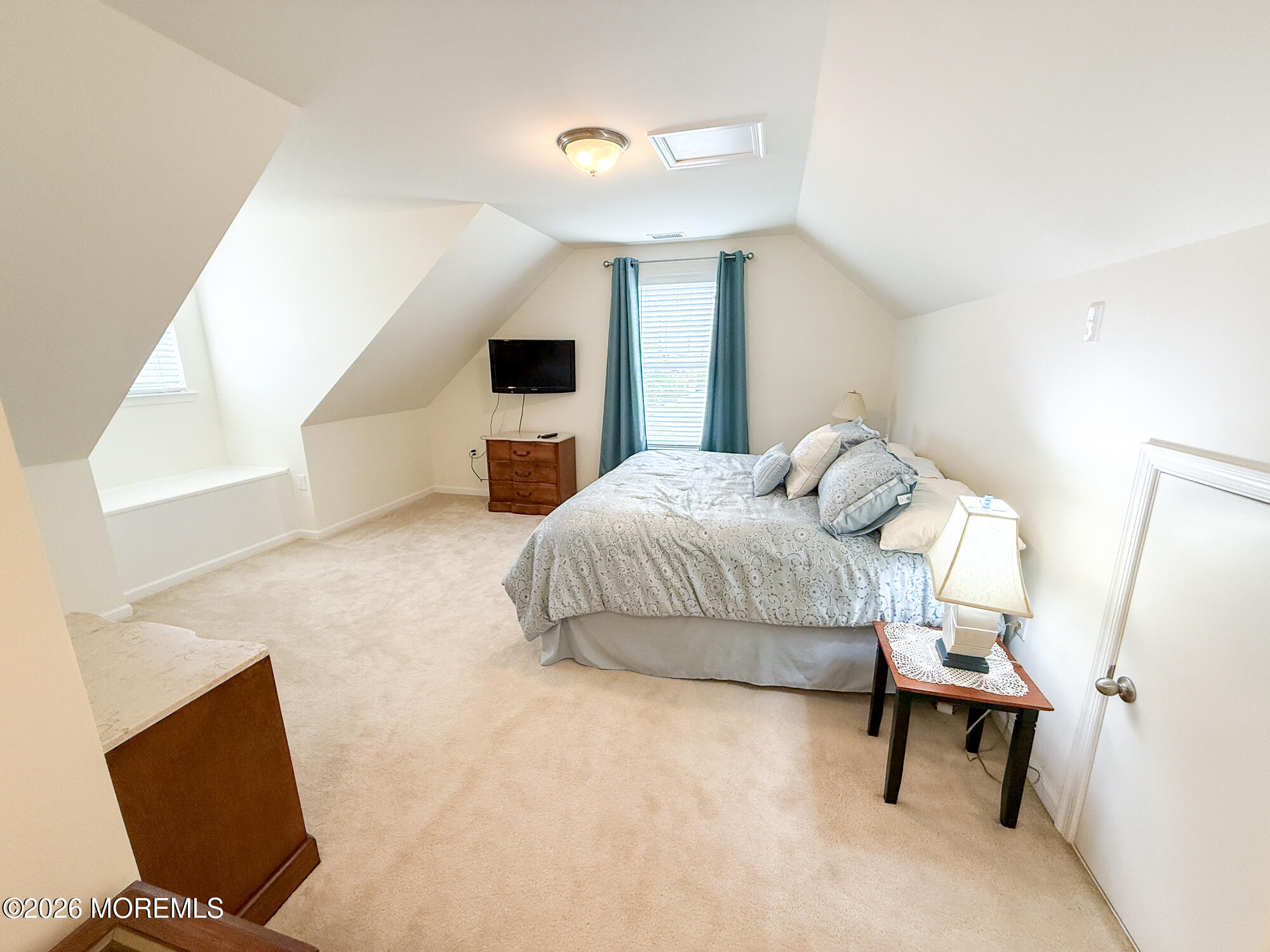 Furnished bedroom with a sloped ceiling, patterned bed, teal curtains, and beige carpeting.