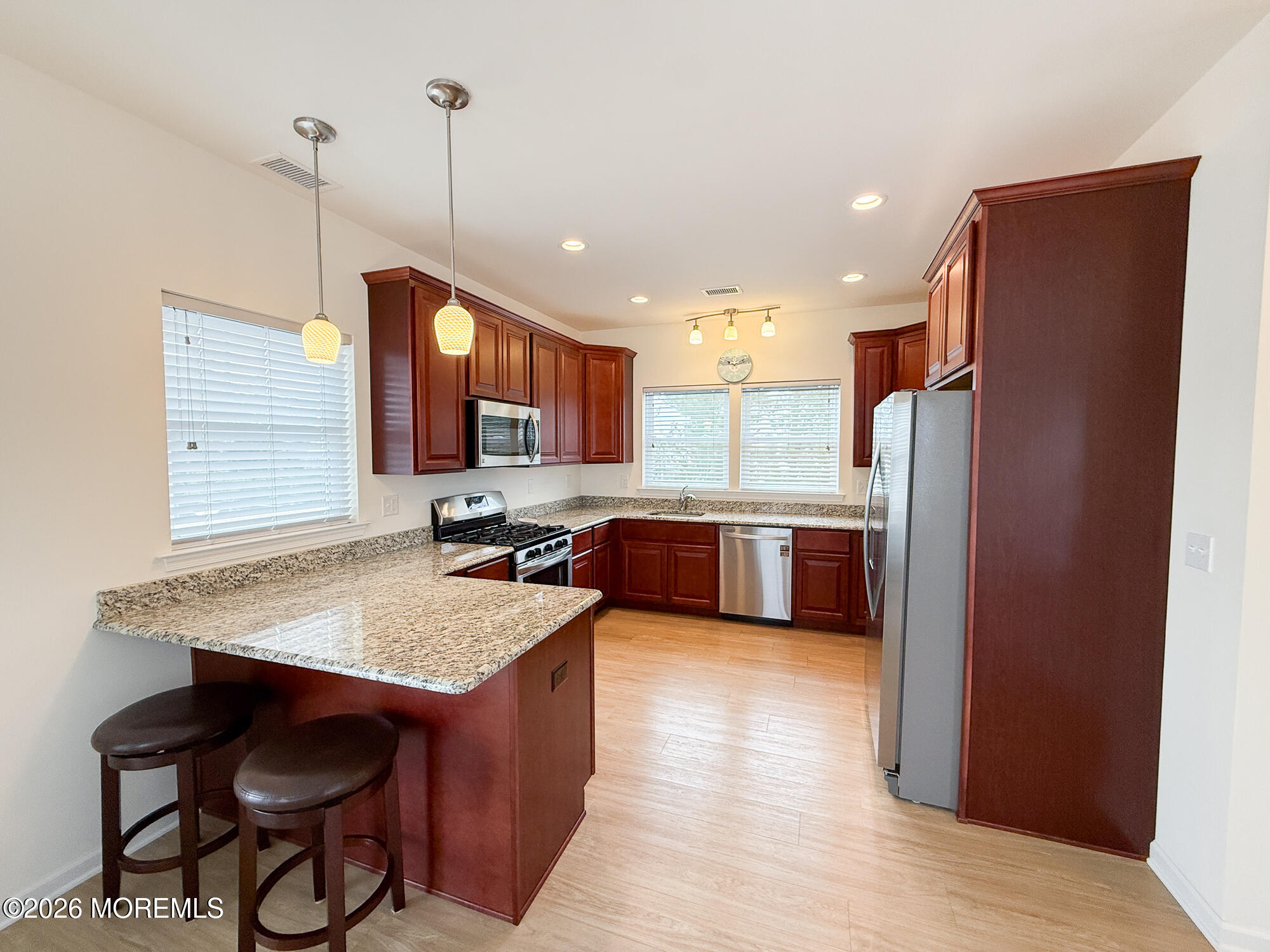 Kitchen with dark wood cabinets, granite breakfast bar, two stools, and stainless steel appliances.
