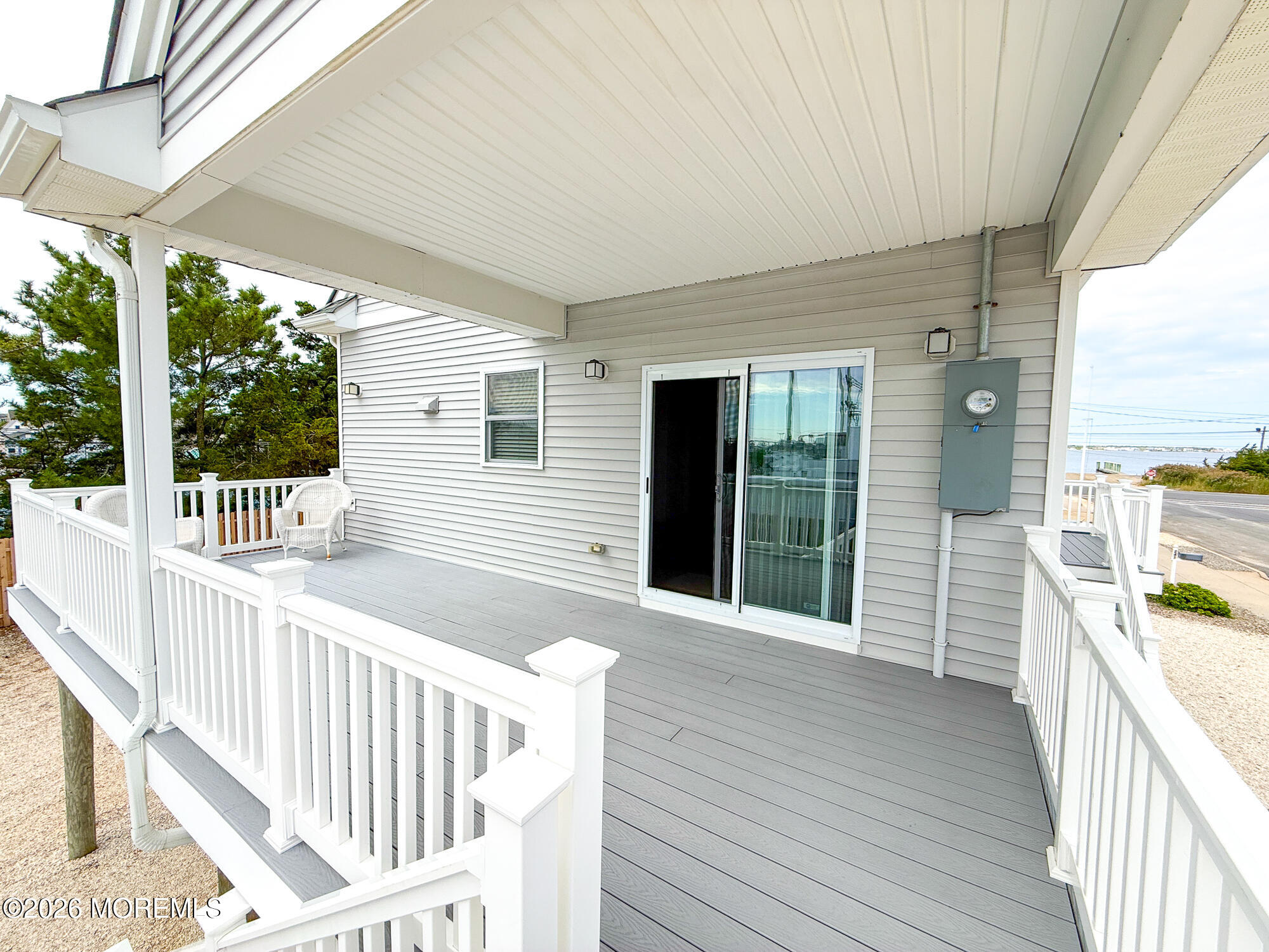 Covered raised deck with gray flooring, white railings, and a view of the water beyond.