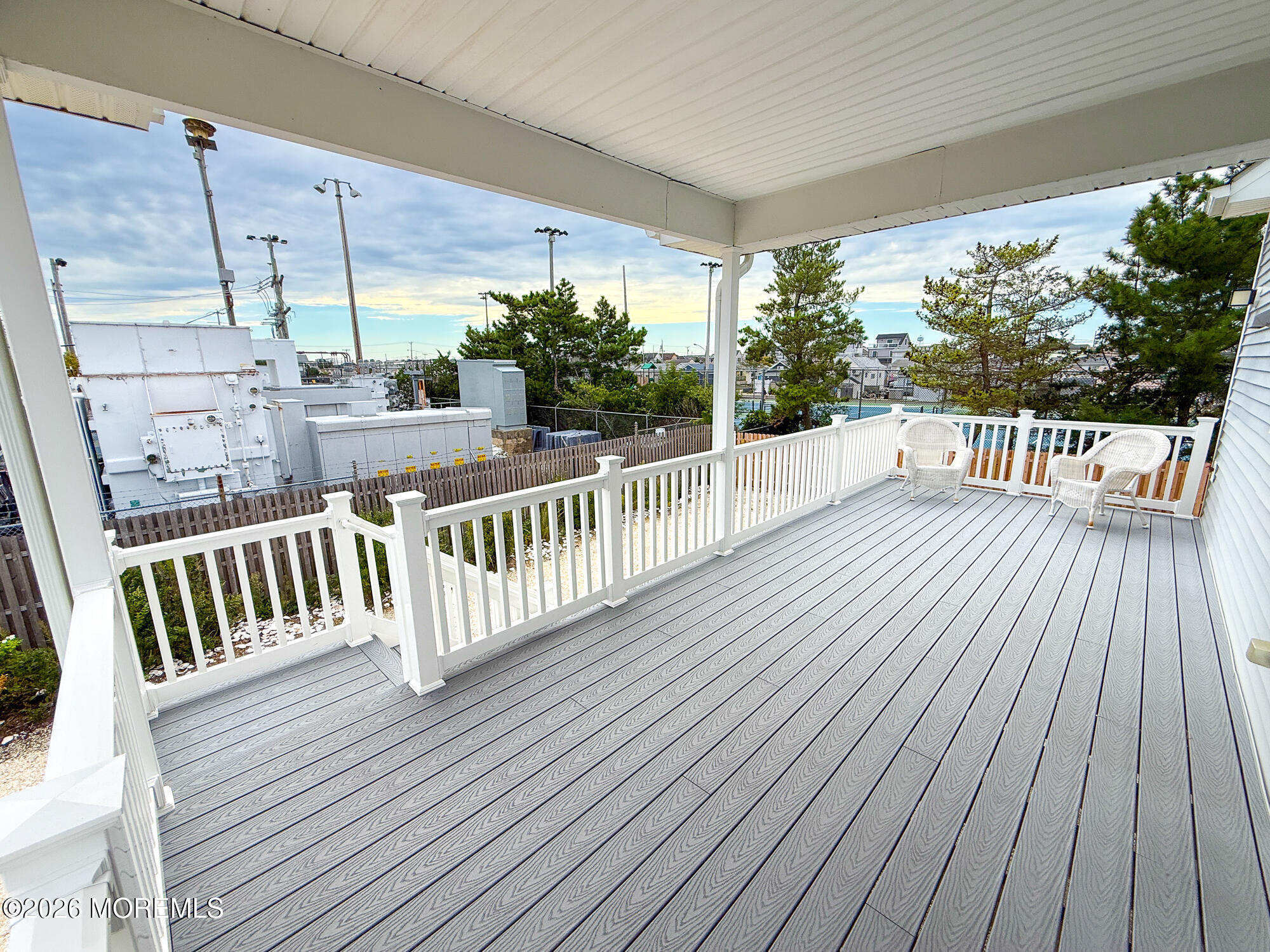 Covered deck with gray composite flooring, white railings, and two wicker chairs.