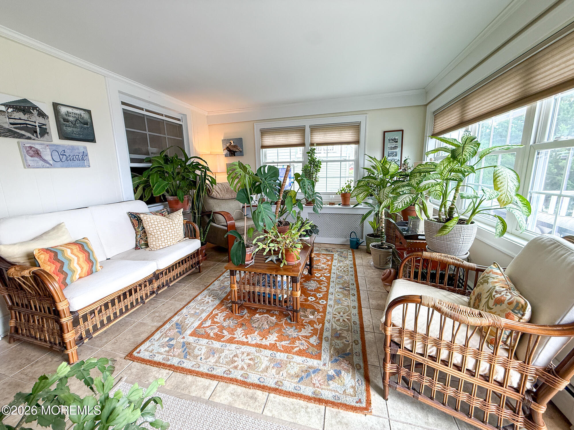 Sunroom with wicker seating, large windows, and numerous potted plants.