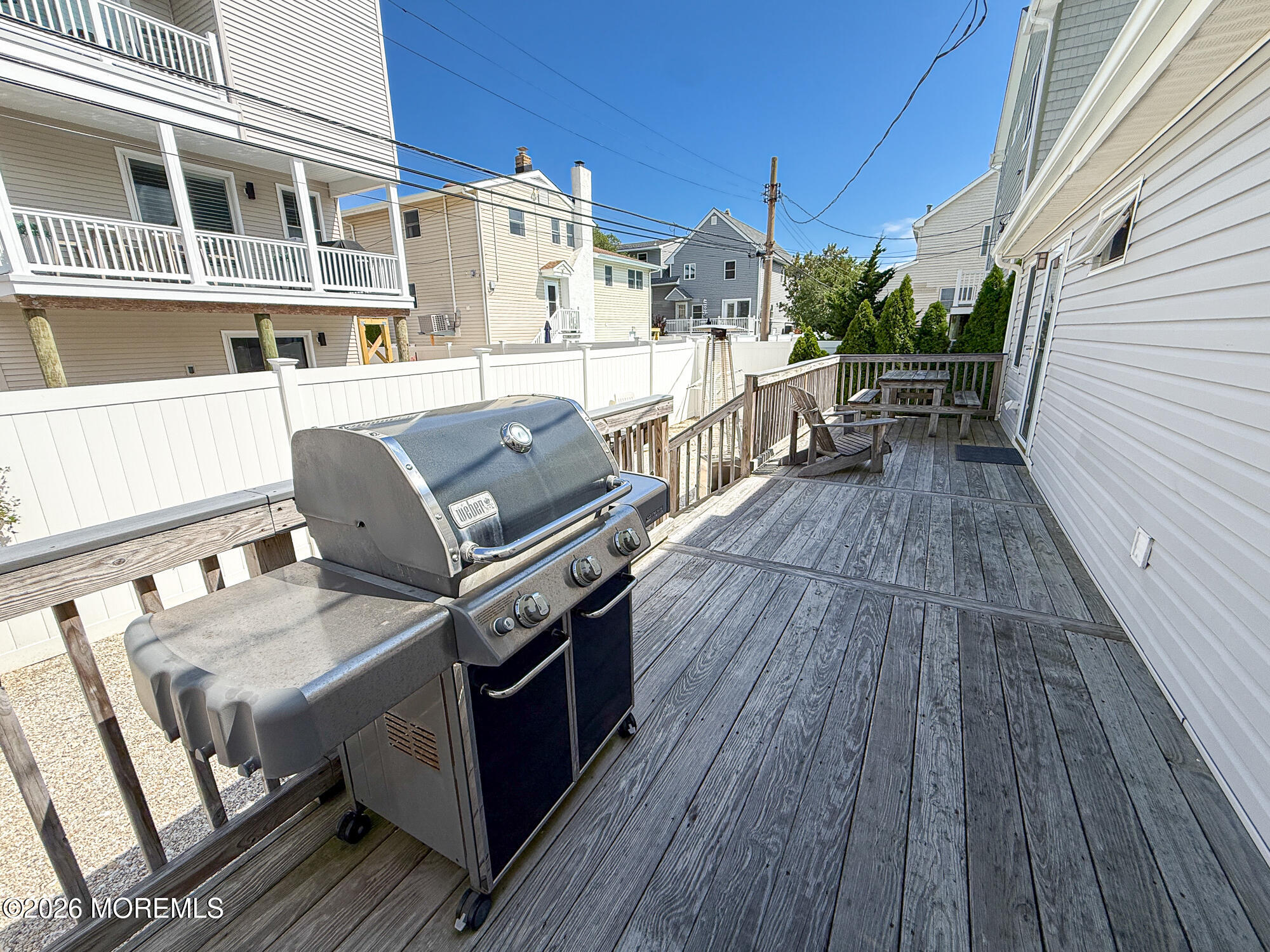 Wood deck with a large gas grill in the foreground and a picnic table at the far end.