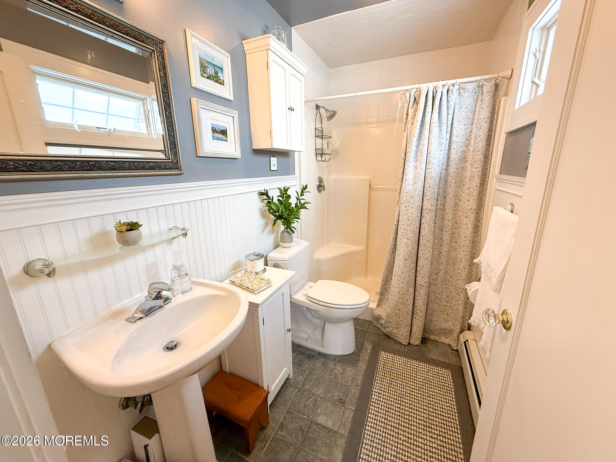 Bathroom with a pedestal sink, toilet, and curtained bathtub, decorated with beadboard and a large mirror.