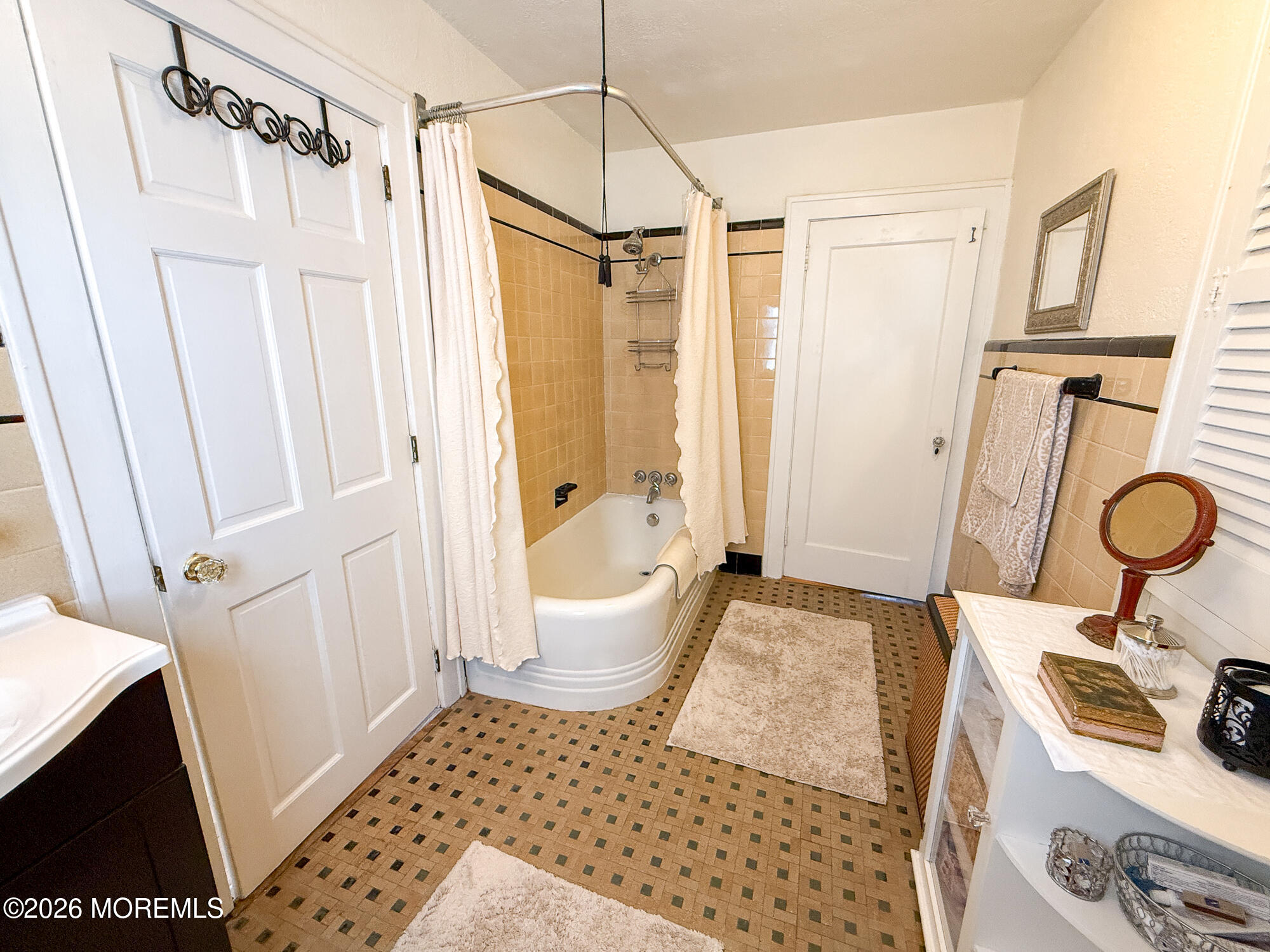 Bathroom with a curtained bathtub, peach tile, patterned mosaic floor, and white vanity.